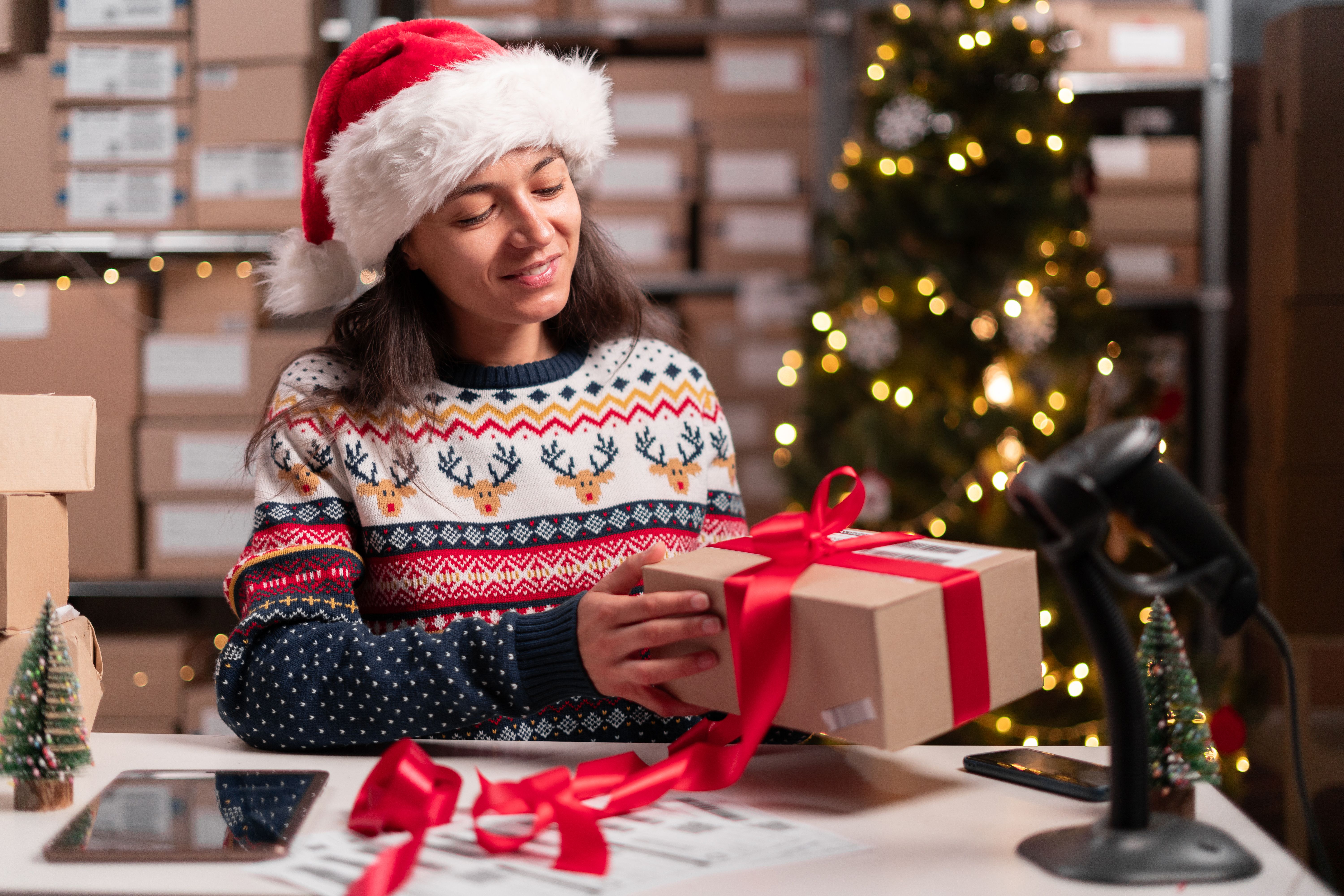 Happy Santa Claus holding present box wrapping with red ribbon preparing post shipping delivery parcel on table in warehouse. Merry Christmas shipping delivery concept.