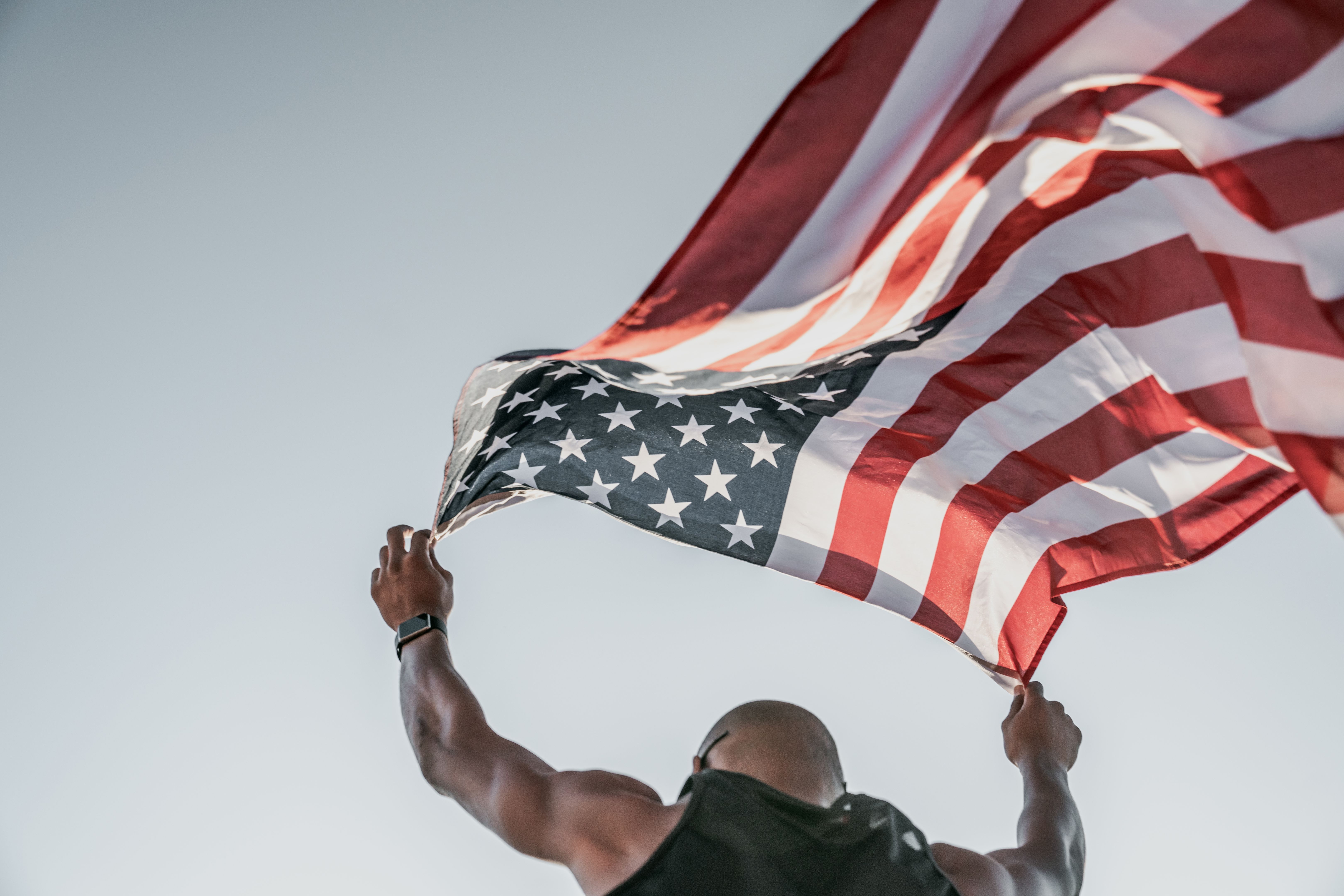 Low angle view of an athlete running on athletic track holding the american flag over the head