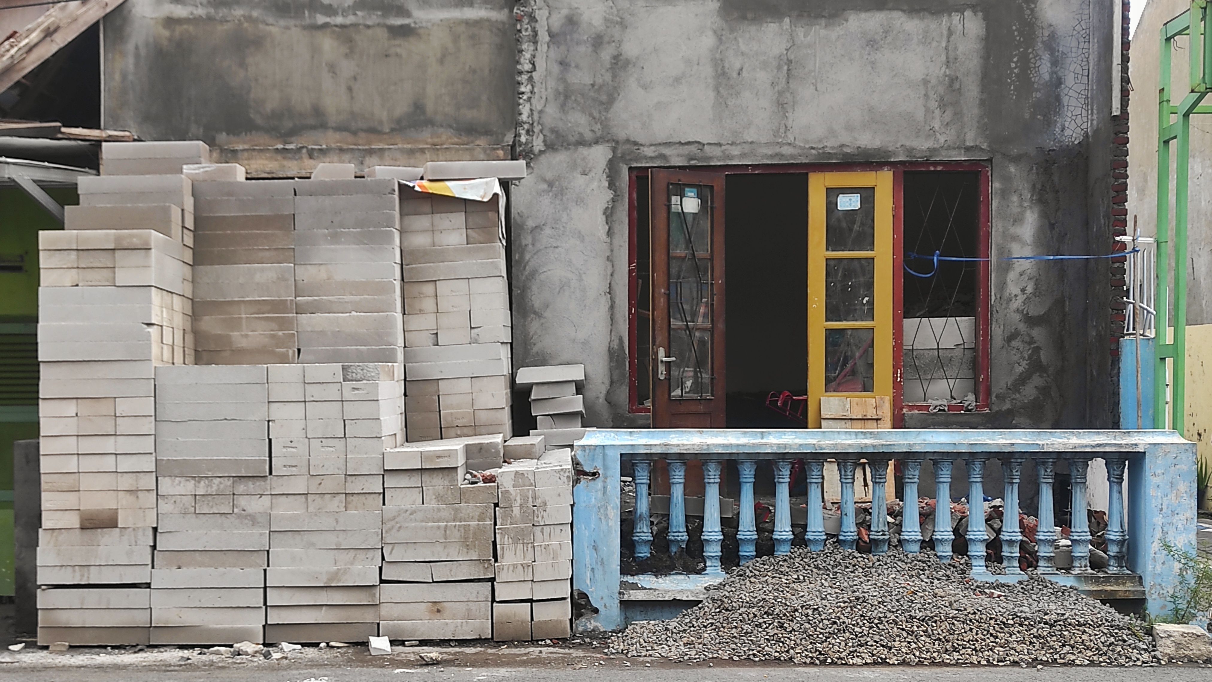 Stacks of concrete bricks and gravel are prepared in front of an old house under renovation. The unfinished structure shows exposed walls and windows, indicating ongoing construction. Stacks of concrete bricks and gravel are prepared in front of an old house under renovation. The unfinished structure shows exposed walls and windows, indicating ongoing construction.