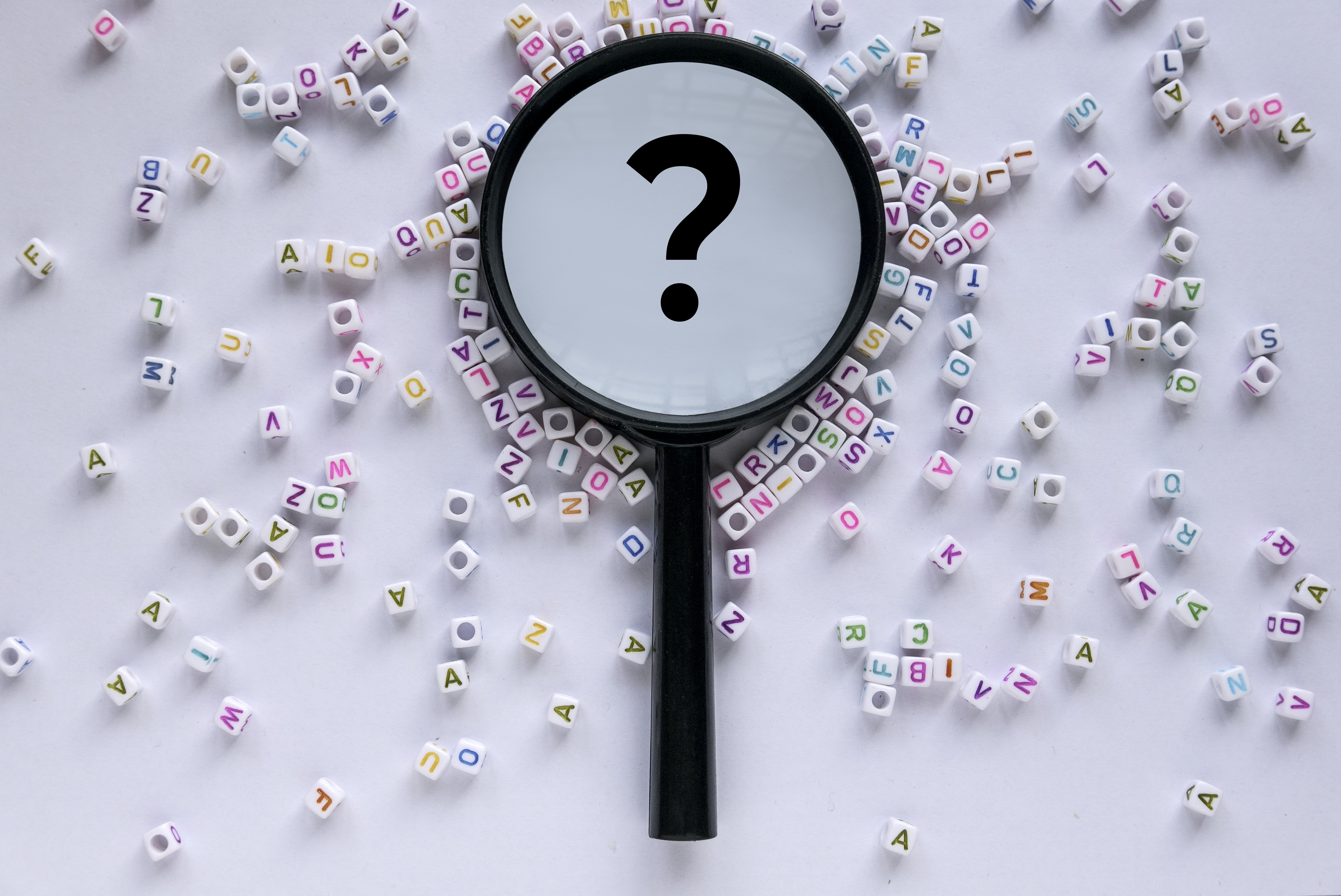 Questions and answers concept. Alphabet beads with magnifying glass with question symbol in it on white background.
