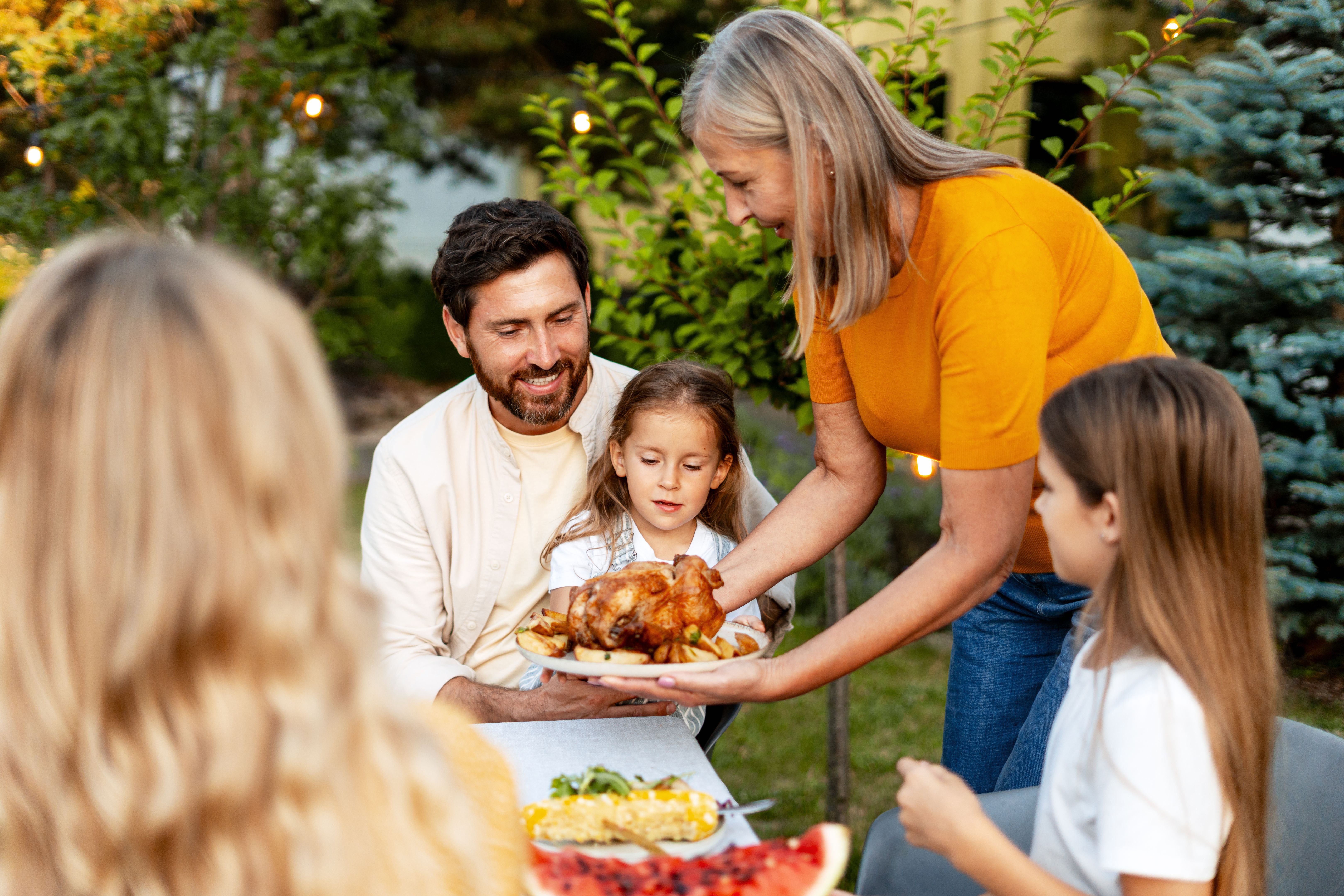 Grandmother serving roasted chicken to family at garden party Grandmother serving roasted chicken to family at garden party