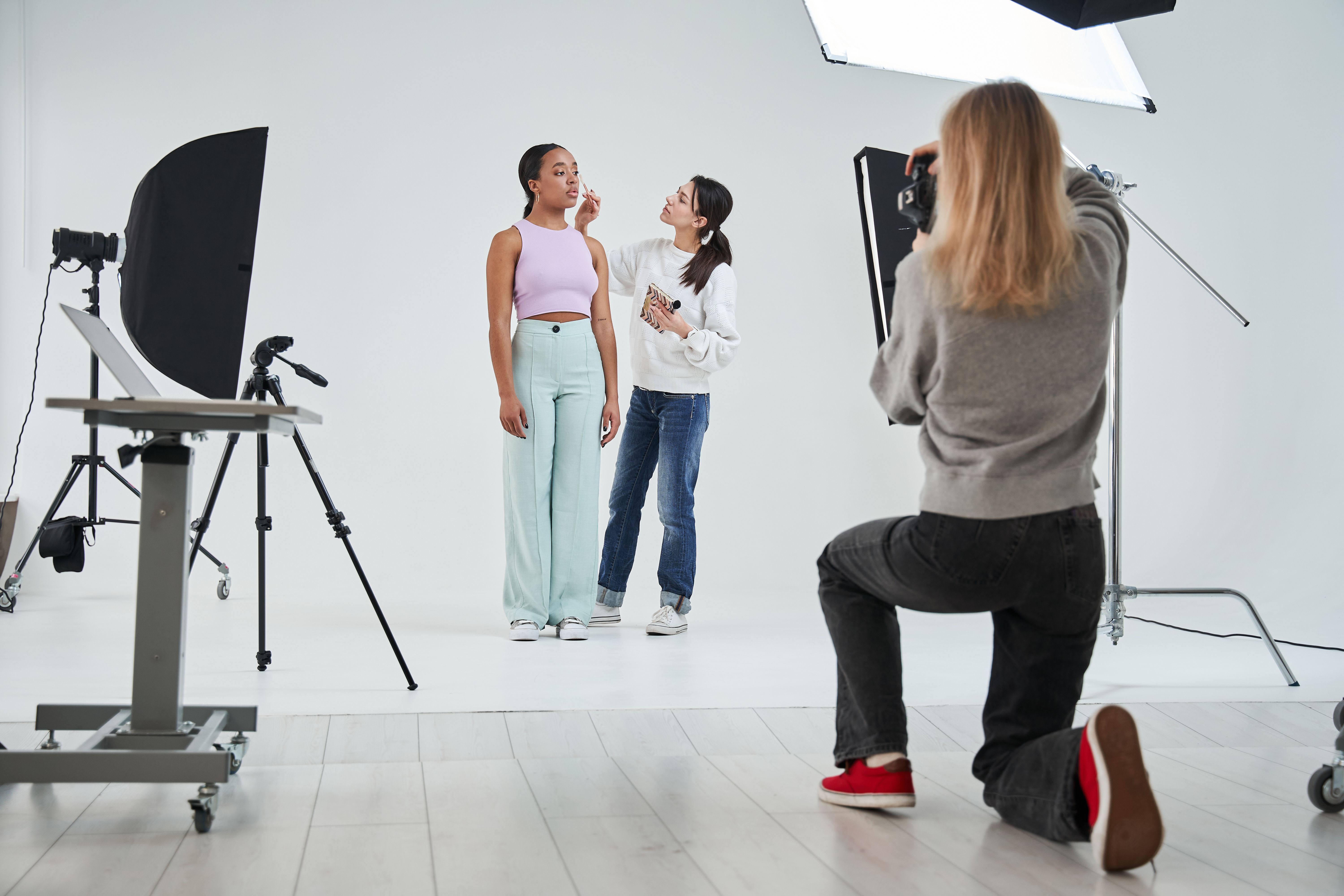 Make-up artist standing near the multiracial model and applying cosmetics