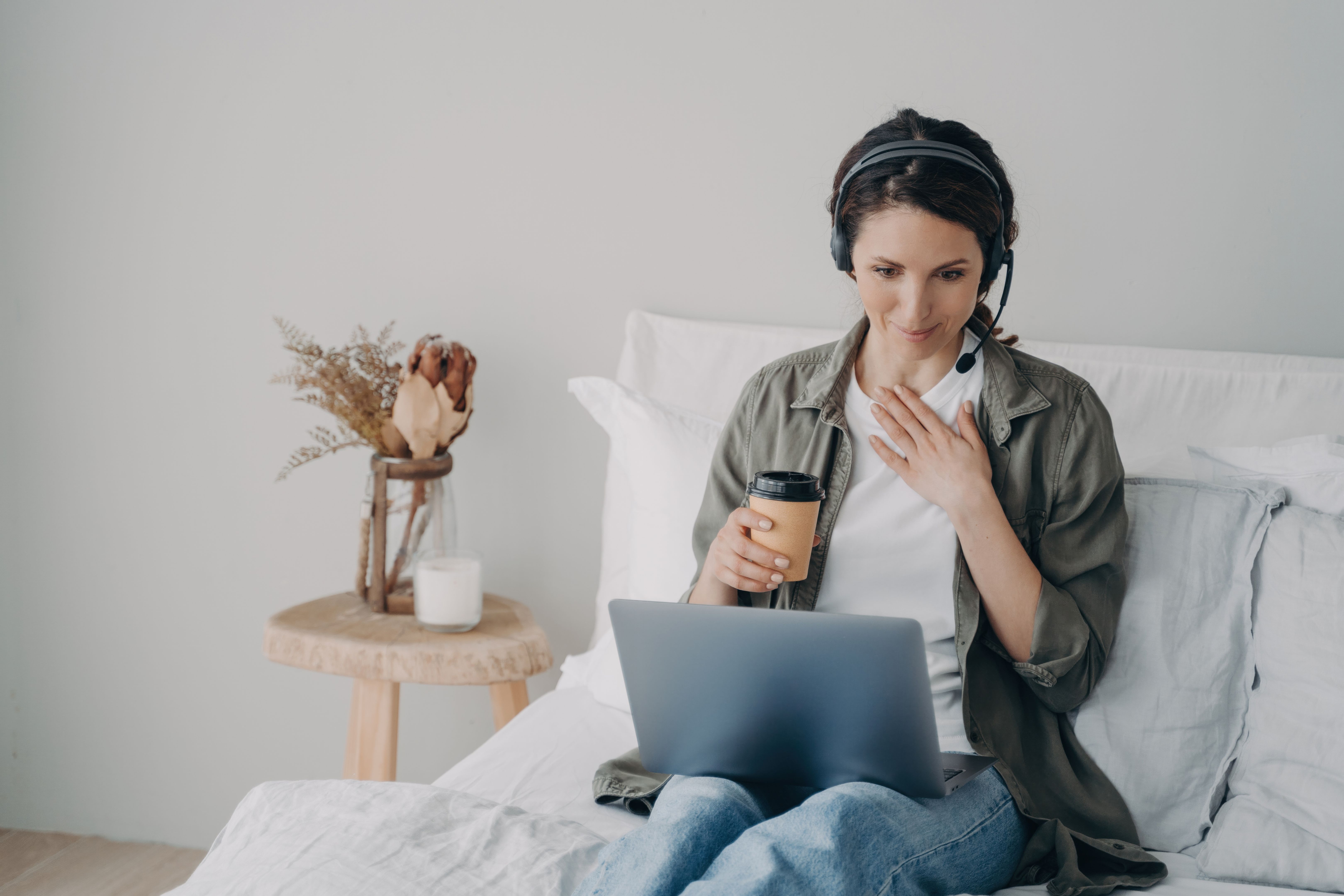 Woman life coach in headset conducts online consultation by video call on laptop in bedroom at home Woman life coach in headset conducts online consultation by video call on laptop in bedroom at home