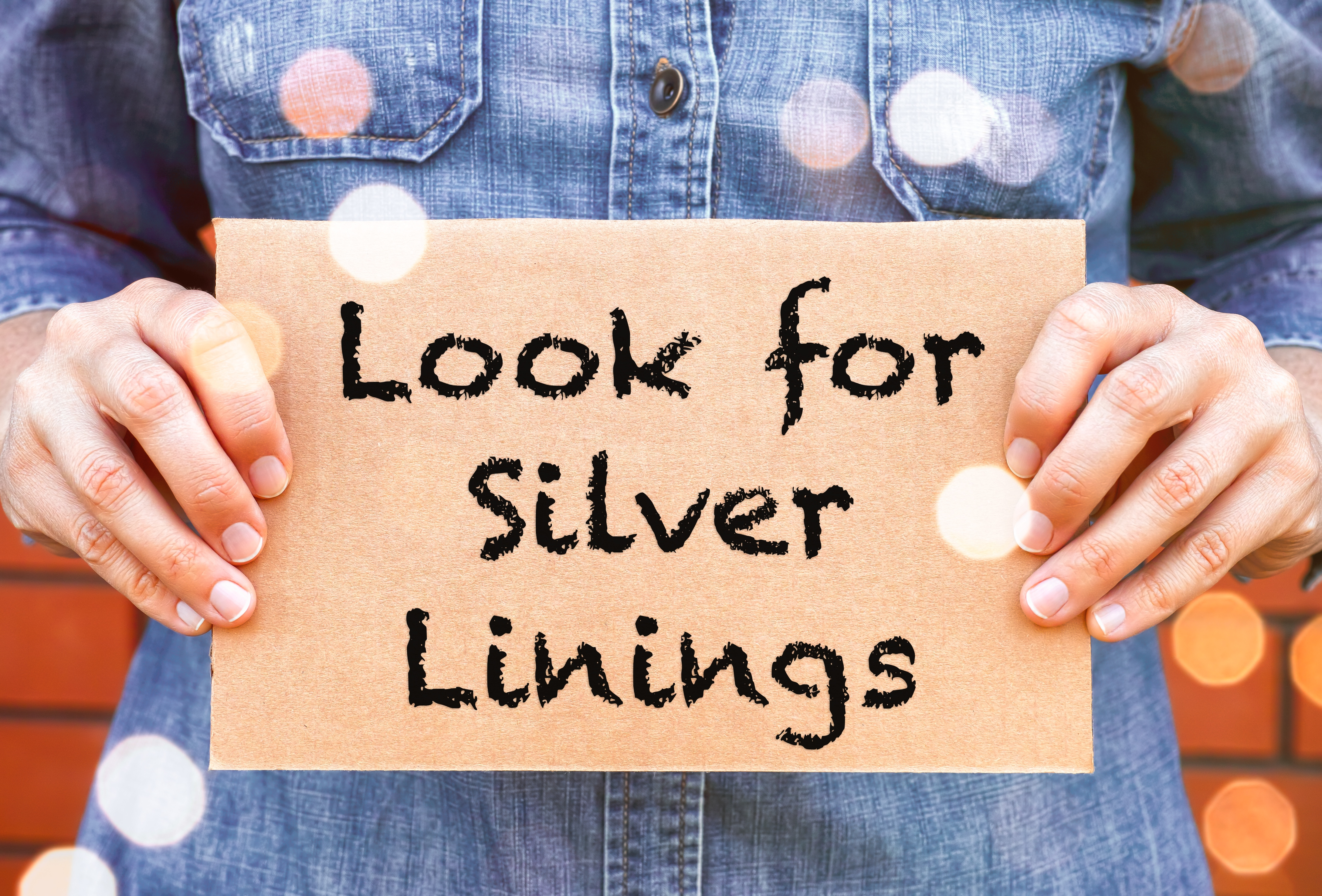 Woman hands holding a piece of a cardboard with words Look for Silver Linings against brick wall background.