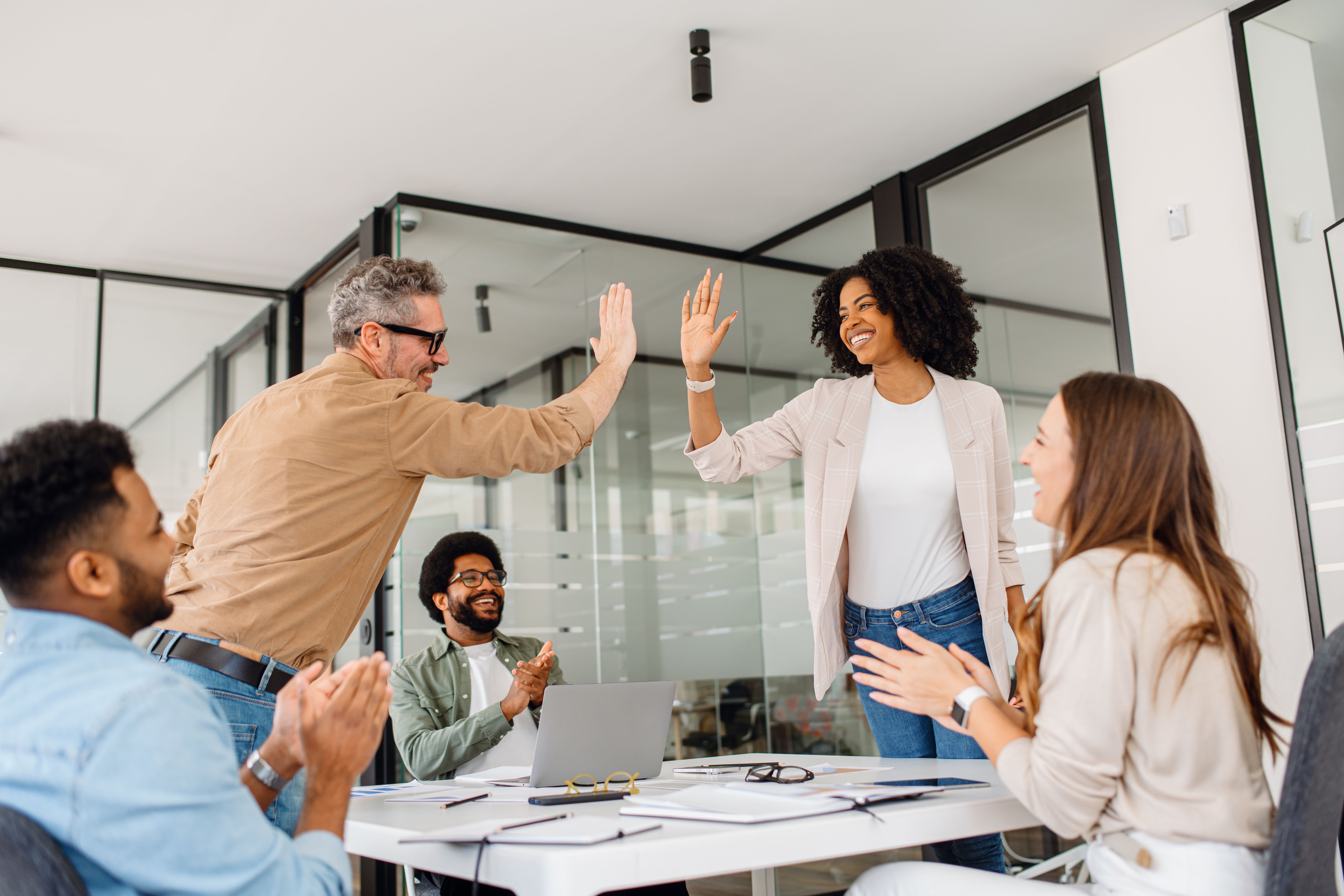 A diverse group of professionals in a modern office celebrates success with a high-five