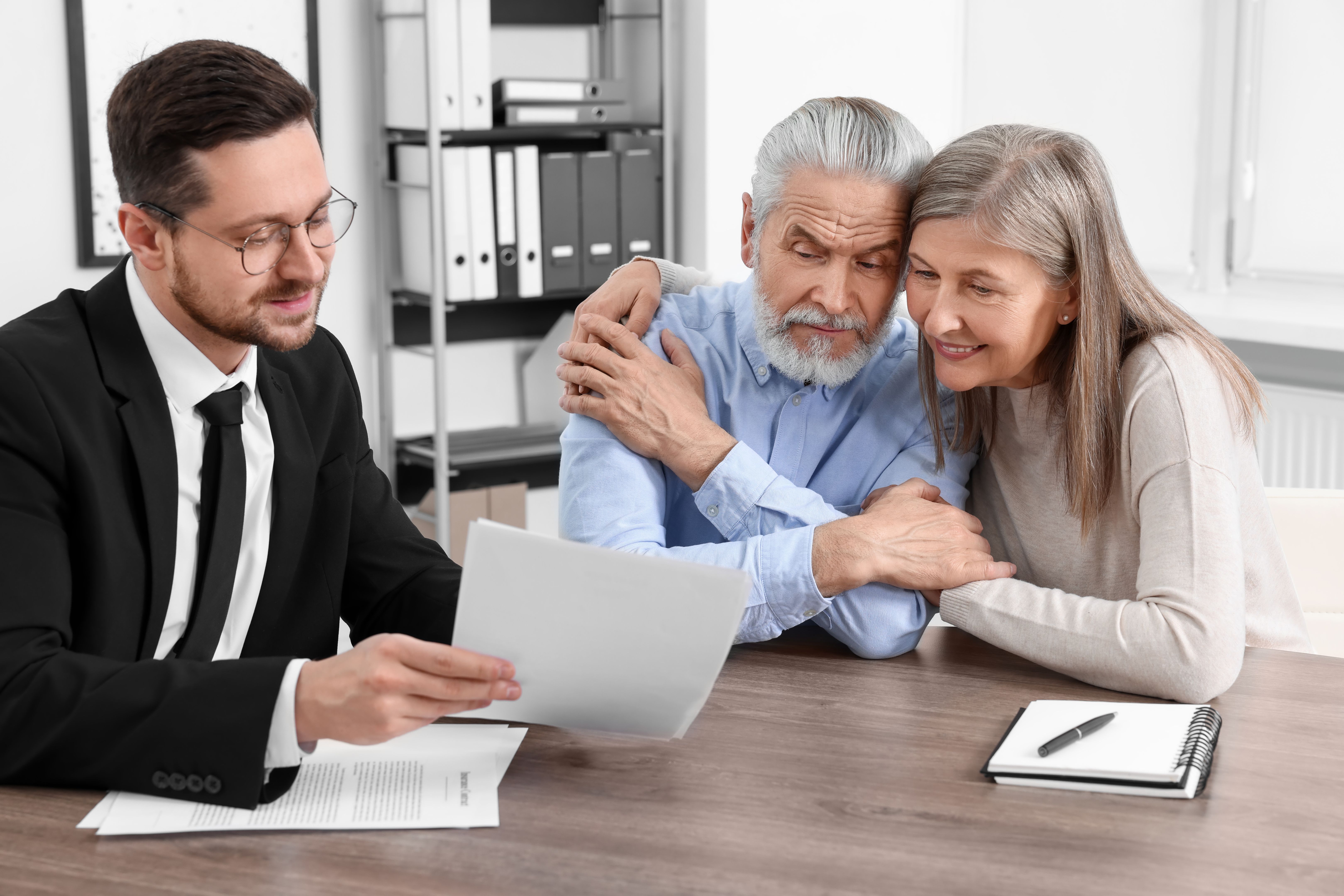 Elderly couple consulting insurance agent about pension plan at wooden table indoors
