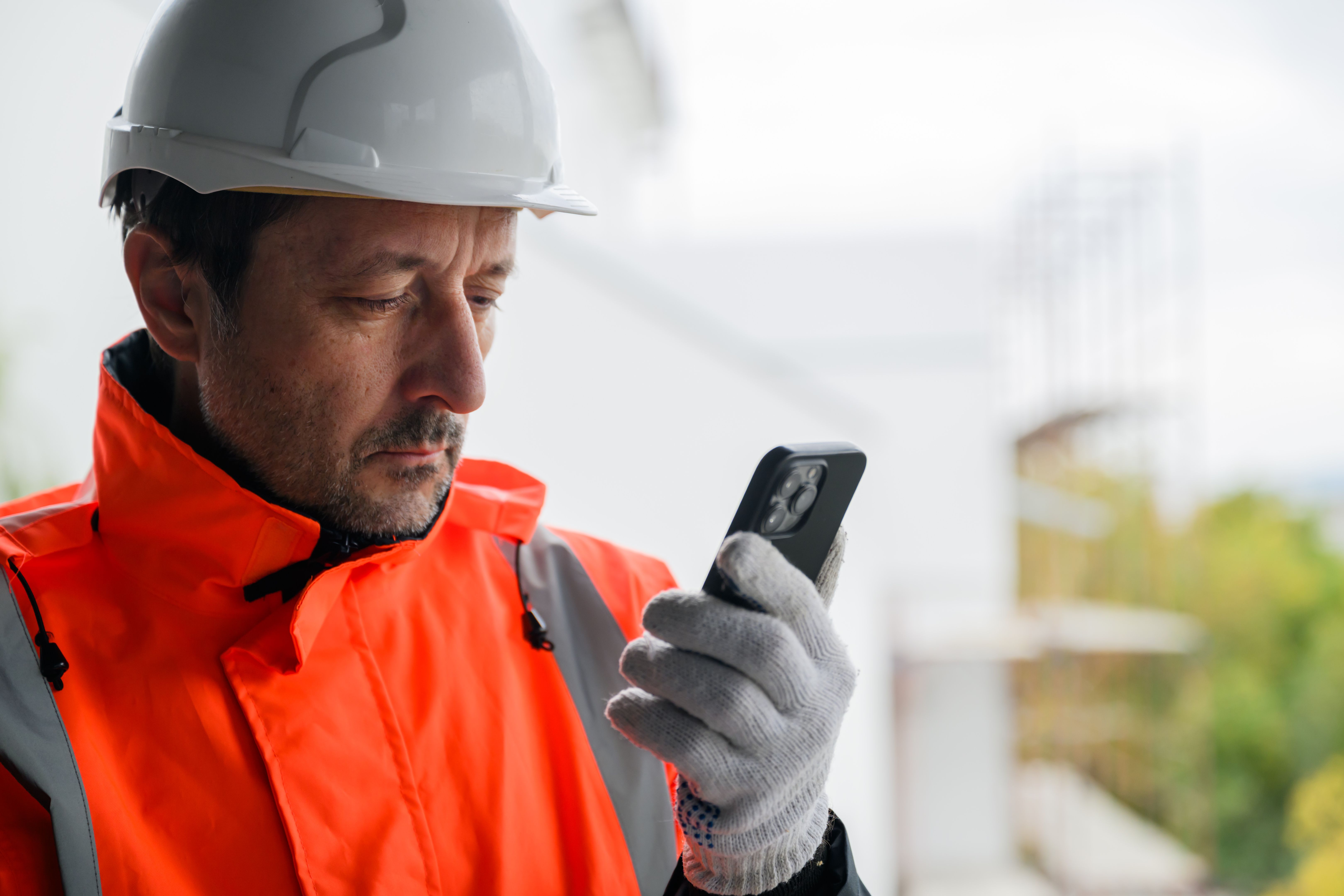 Ingeniero civil con equipo de seguridad usando smartphone en obra, representando comunicación digital, gestión remota y desarrollo de infraestructuras modernas.