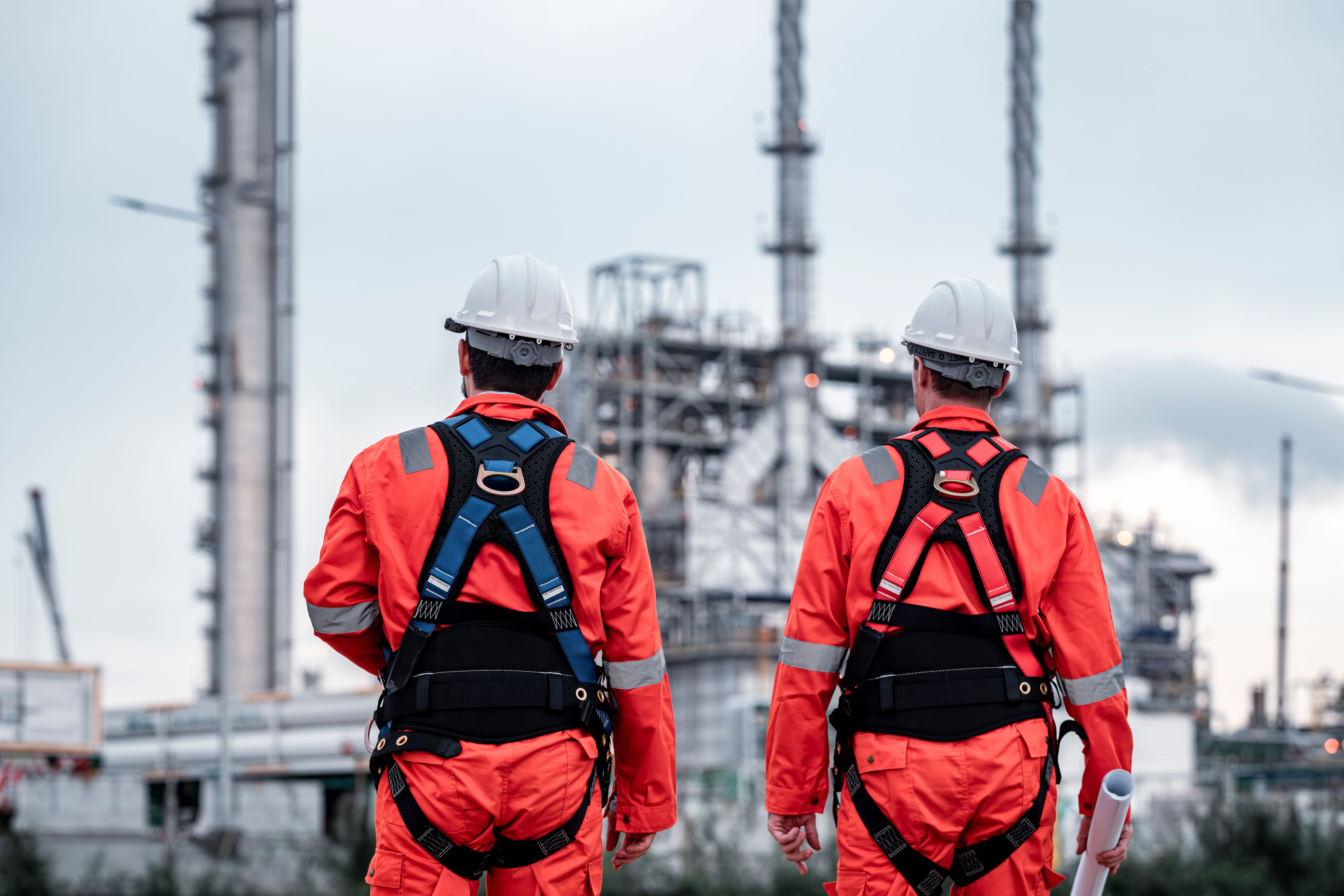 Engineer survey team wear uniform and helmet stand workplace checking blueprint project , radio communication and engineer box inspection work construction site with oil refinery background.