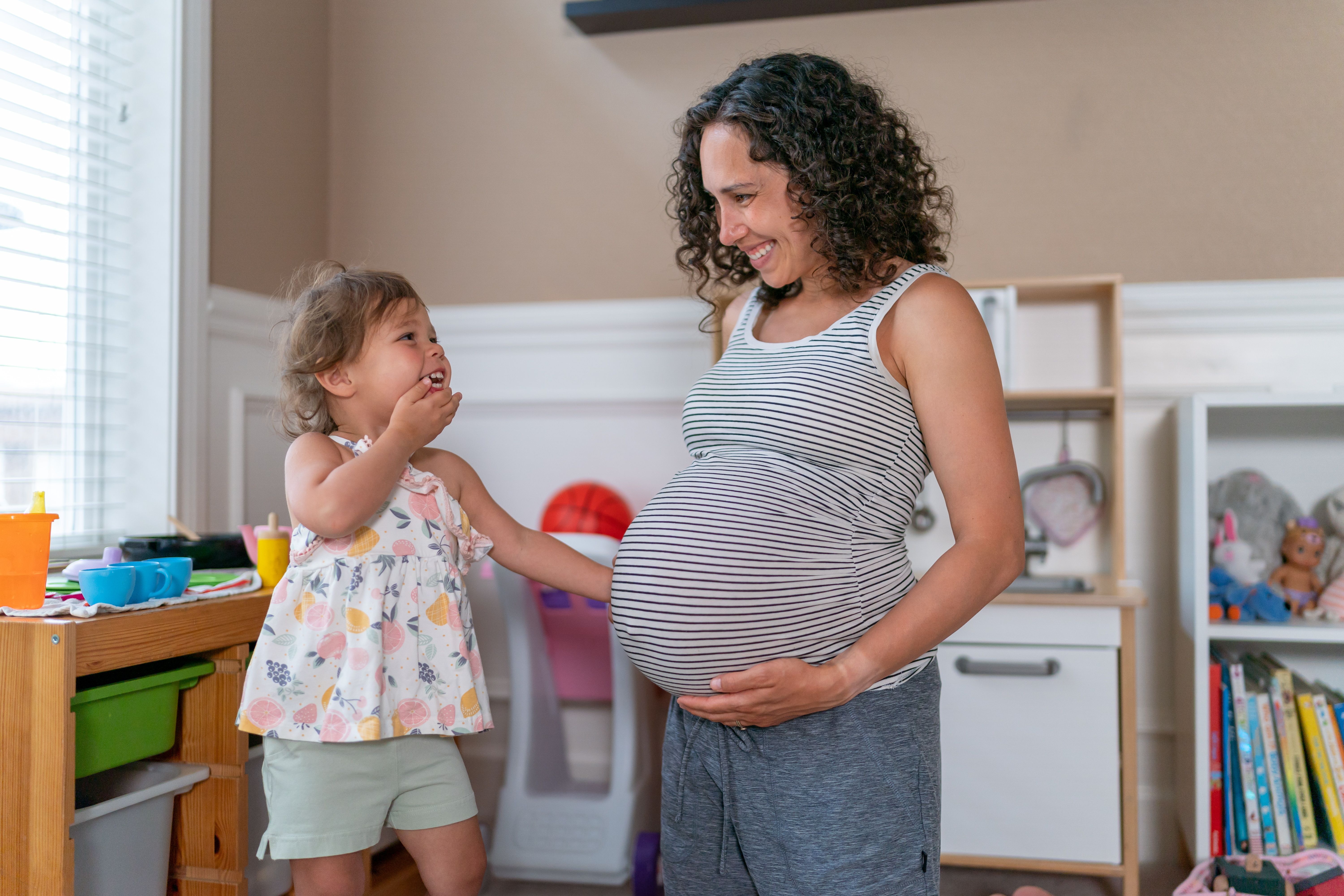 A pregnant ethnic mother and her toddler snuggling in their home playroom