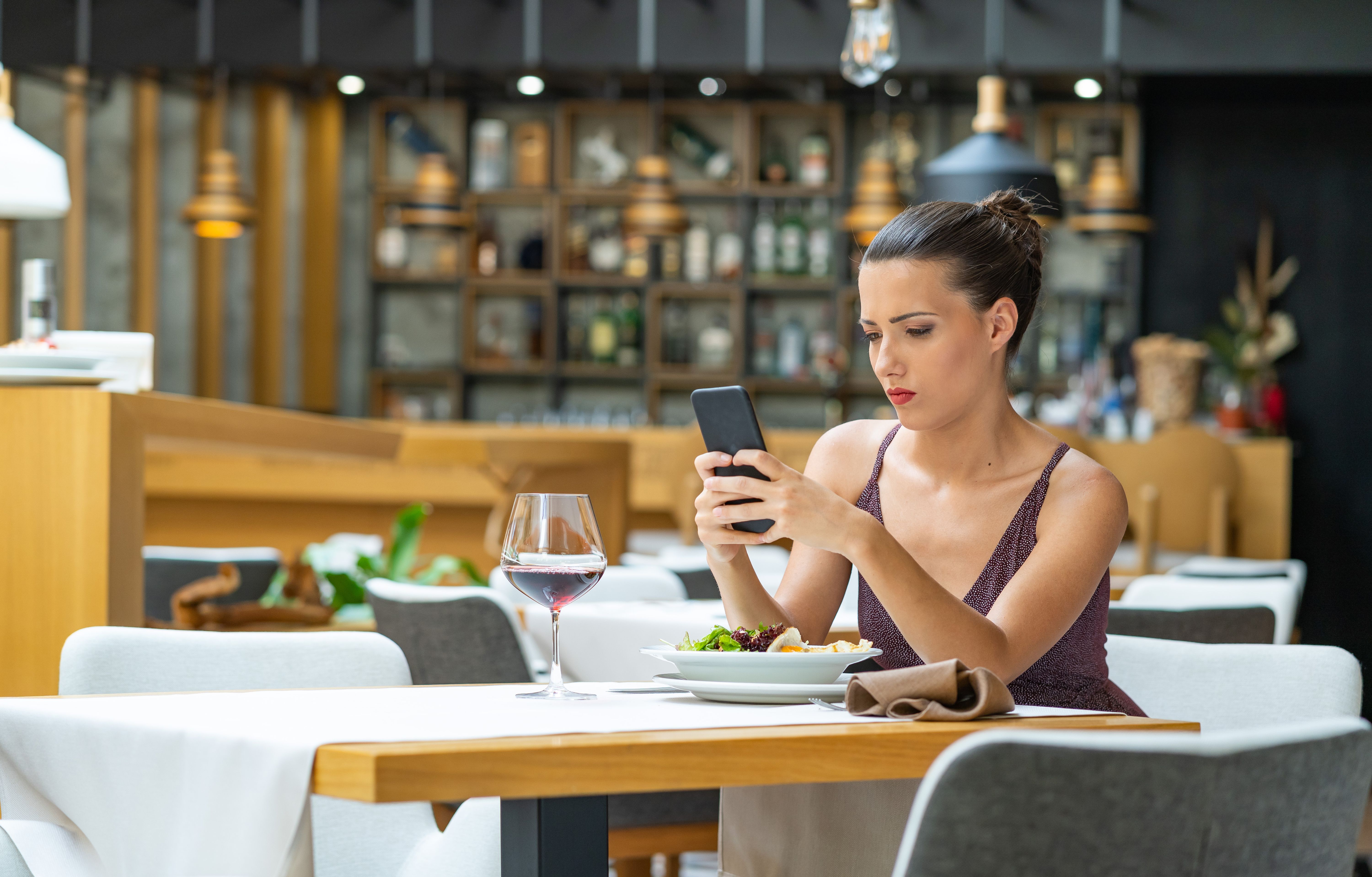 Sad woman sitting in restaurant and using smart phone