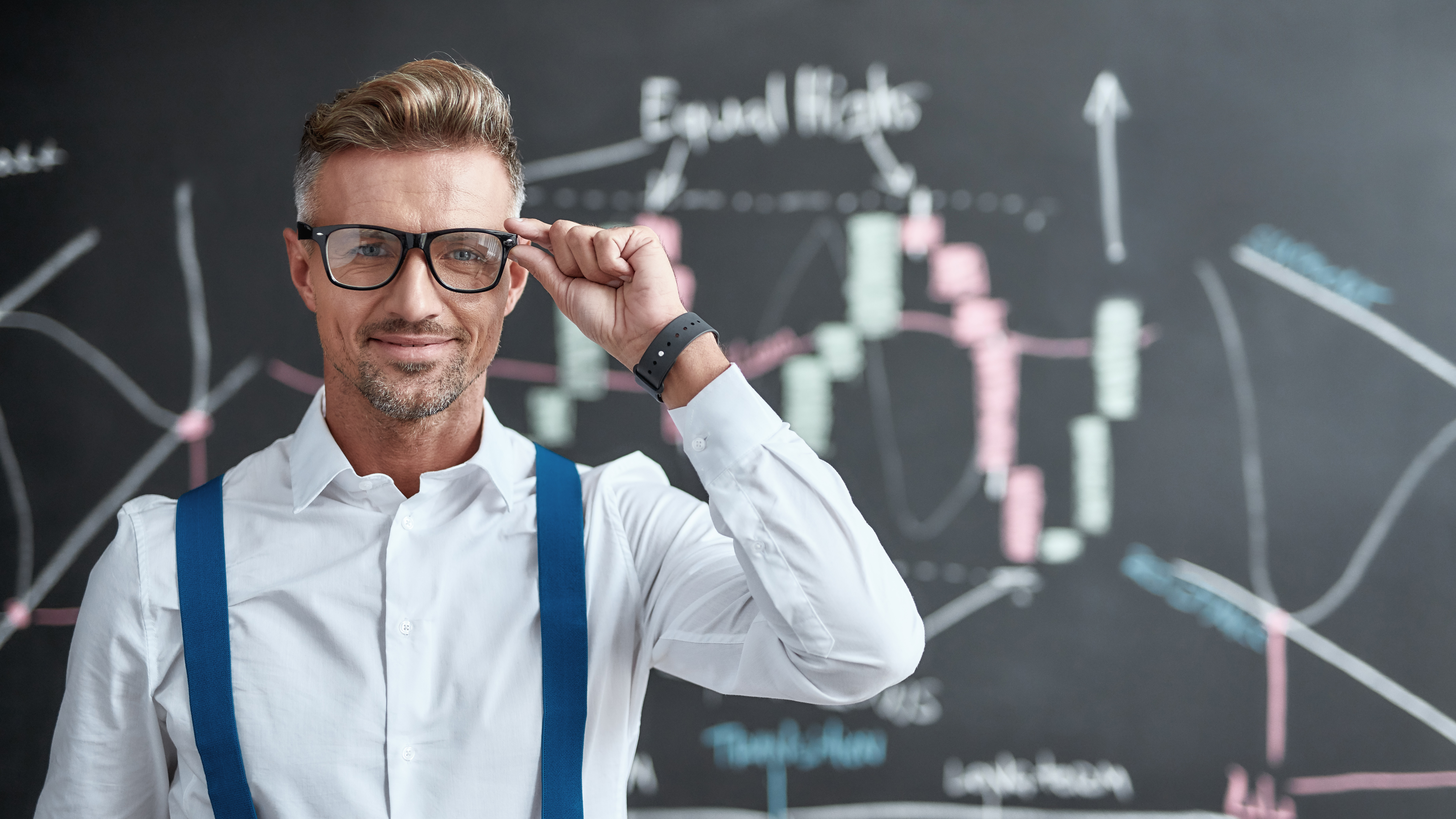 Broking for the source of income of tomorrow. Close up of middle-aged trader looking at camera and standing near blackboard full of charts, while thinking of the new strategy of work. Horizontal shot