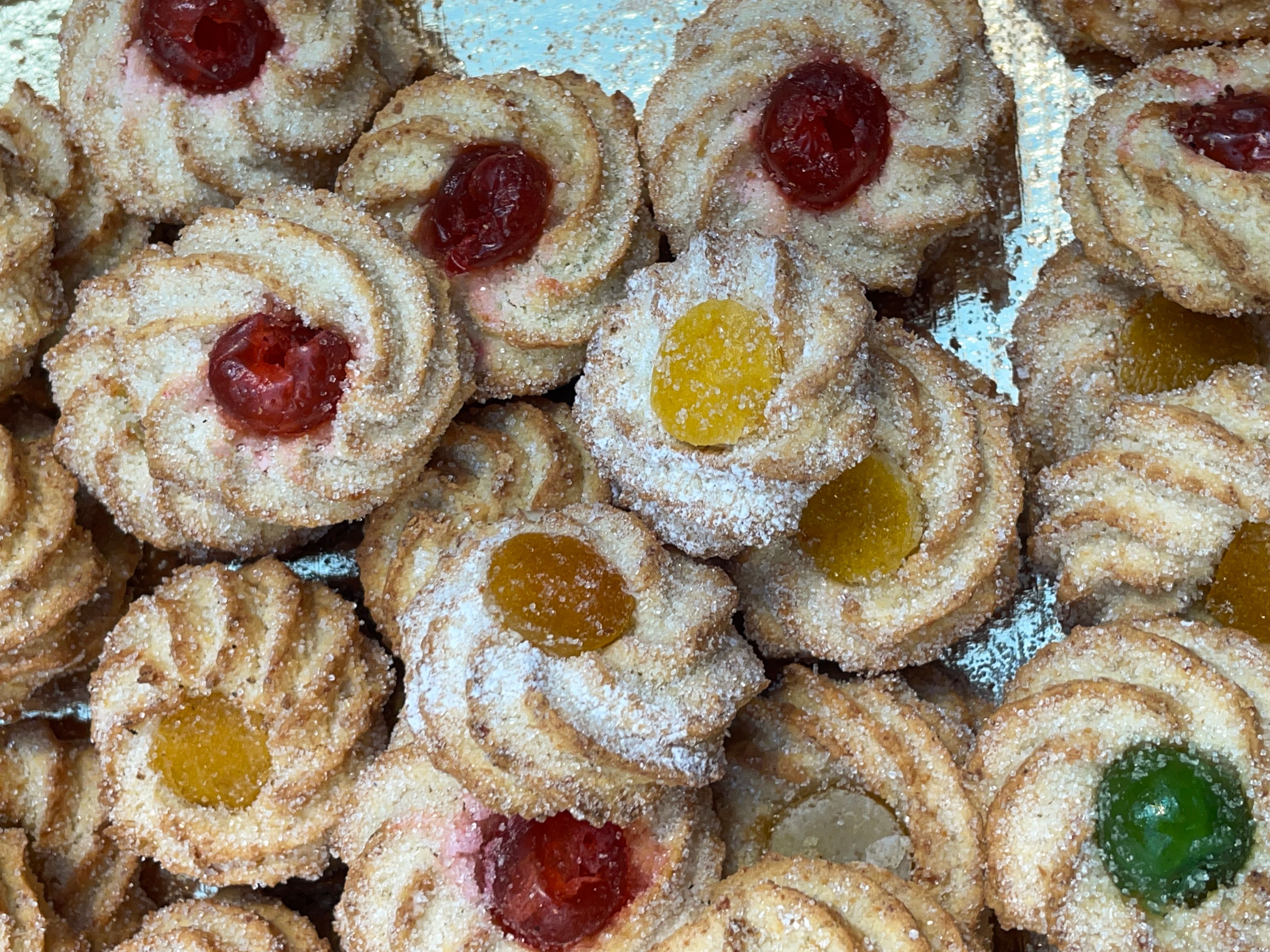 Full frame image of Viennese whirl biscuits decorated with red, yellow or green glace cherries stacked in wooden tray on bakery shelf, traffic light cookies, elevated view