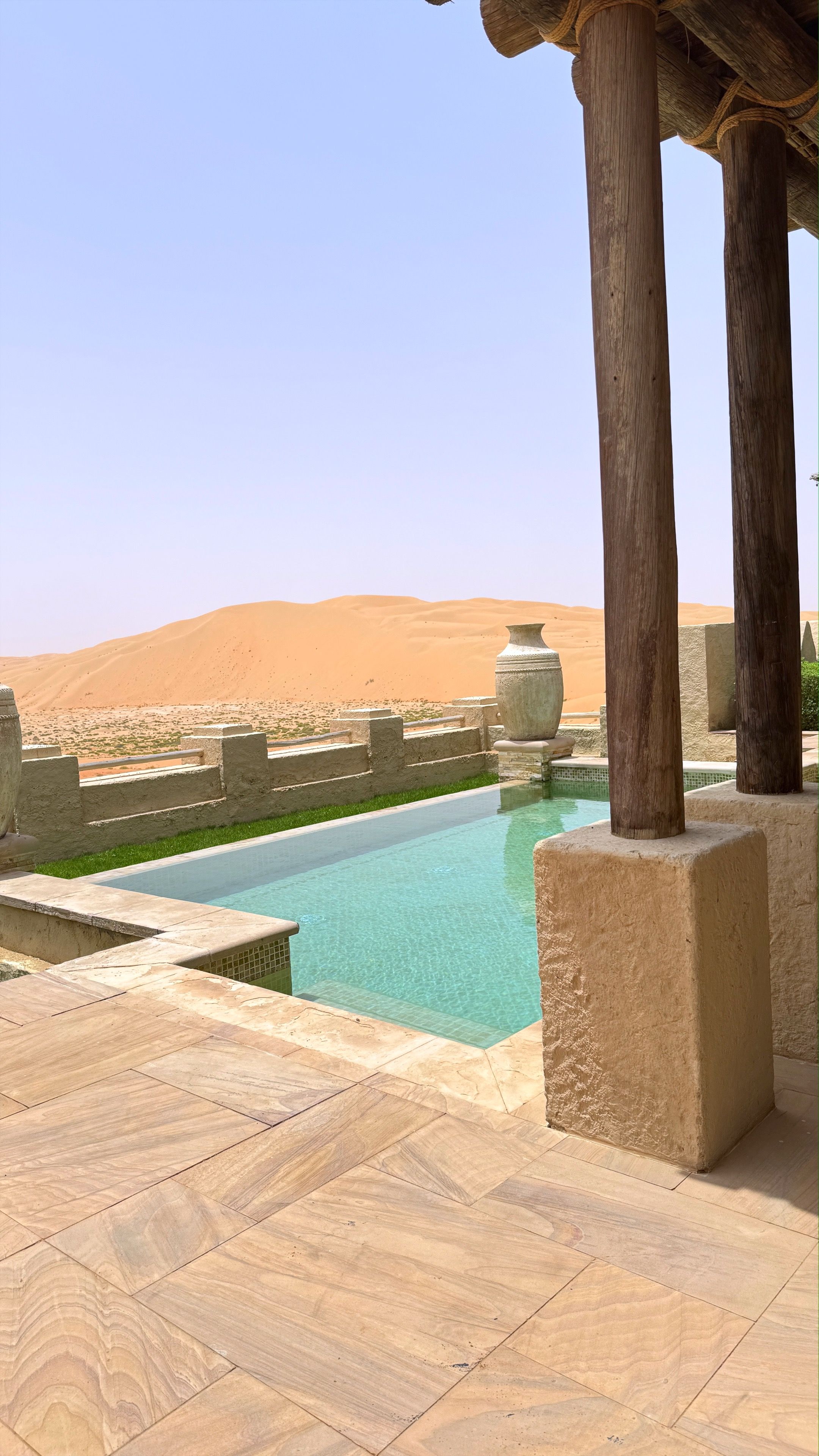 Turquoise swimming pool nestled on stone pavement, wooden pillars framing panoramic desert scenery in luxurious United Arab Emirates resort setting
