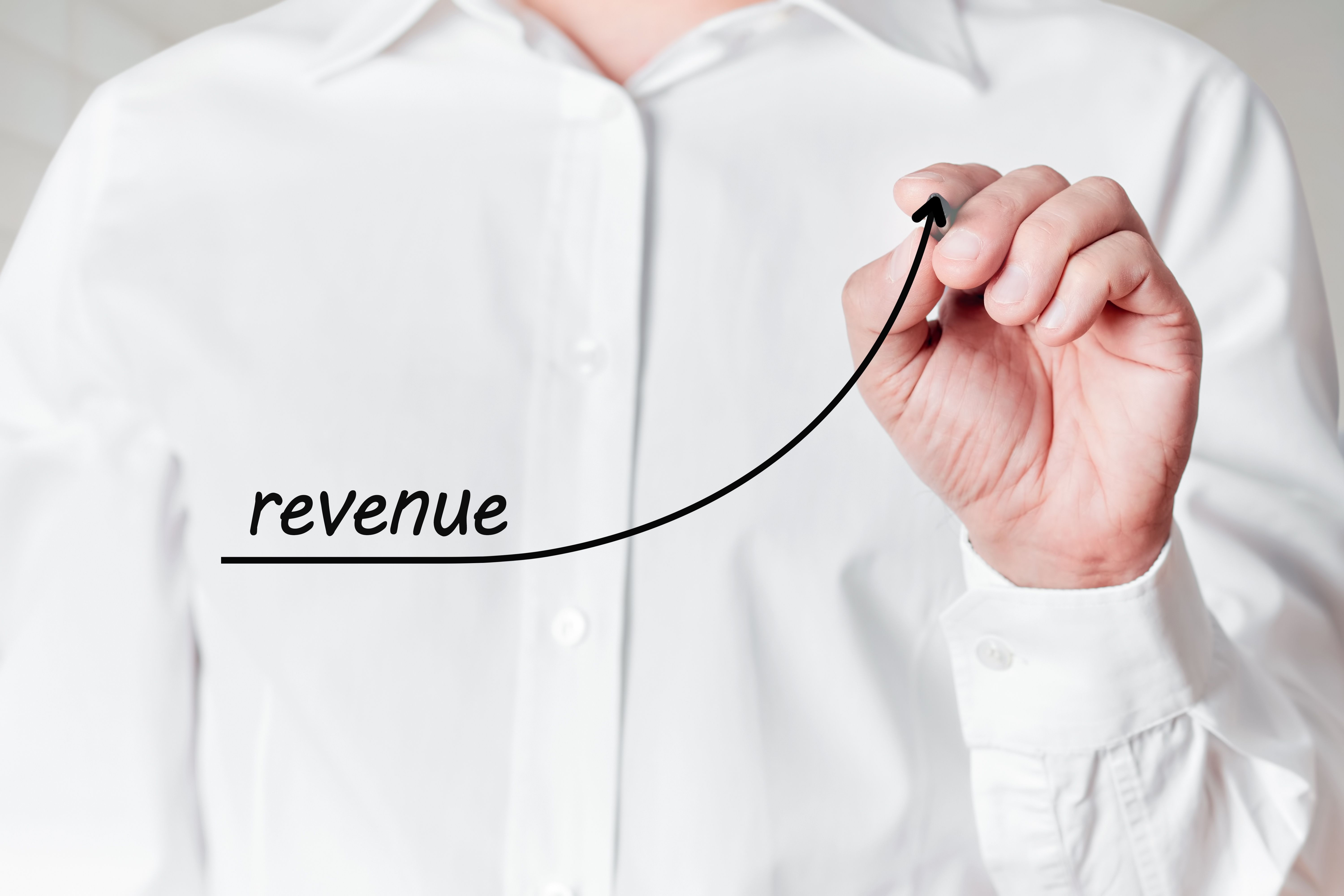 Businessman with a pen draws a rising line graph with the word revenue on a virtual screen. Business revenue increase