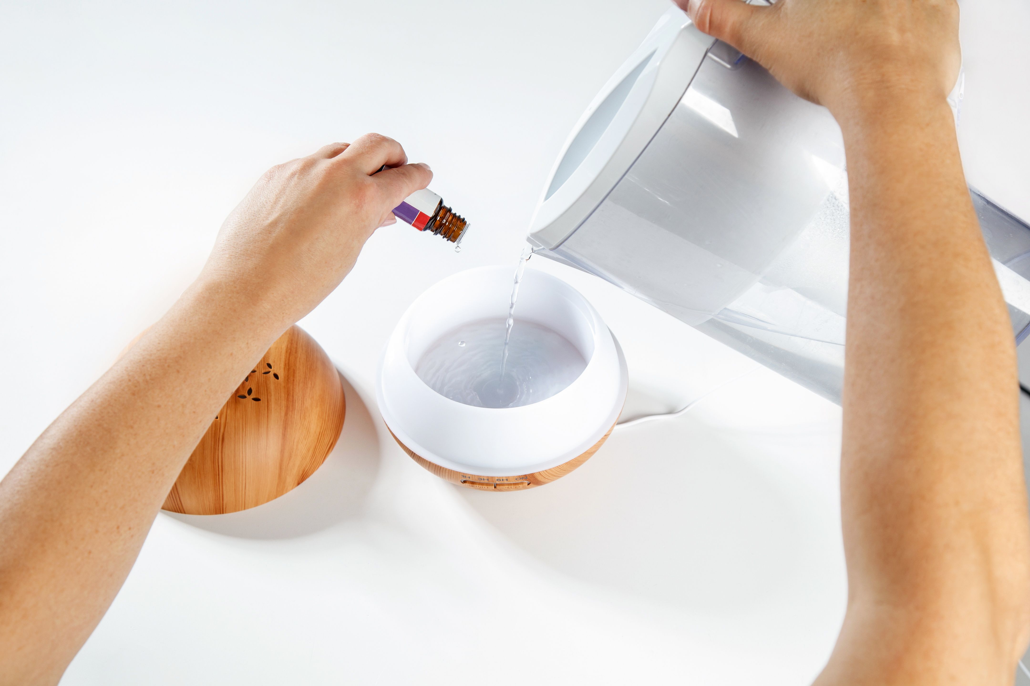 Pouring filtered water and essential oil in aromatherapy diffuser with wooden pattern Pouring filtered water and essential oil in aromatherapy diffuser with wooden pattern