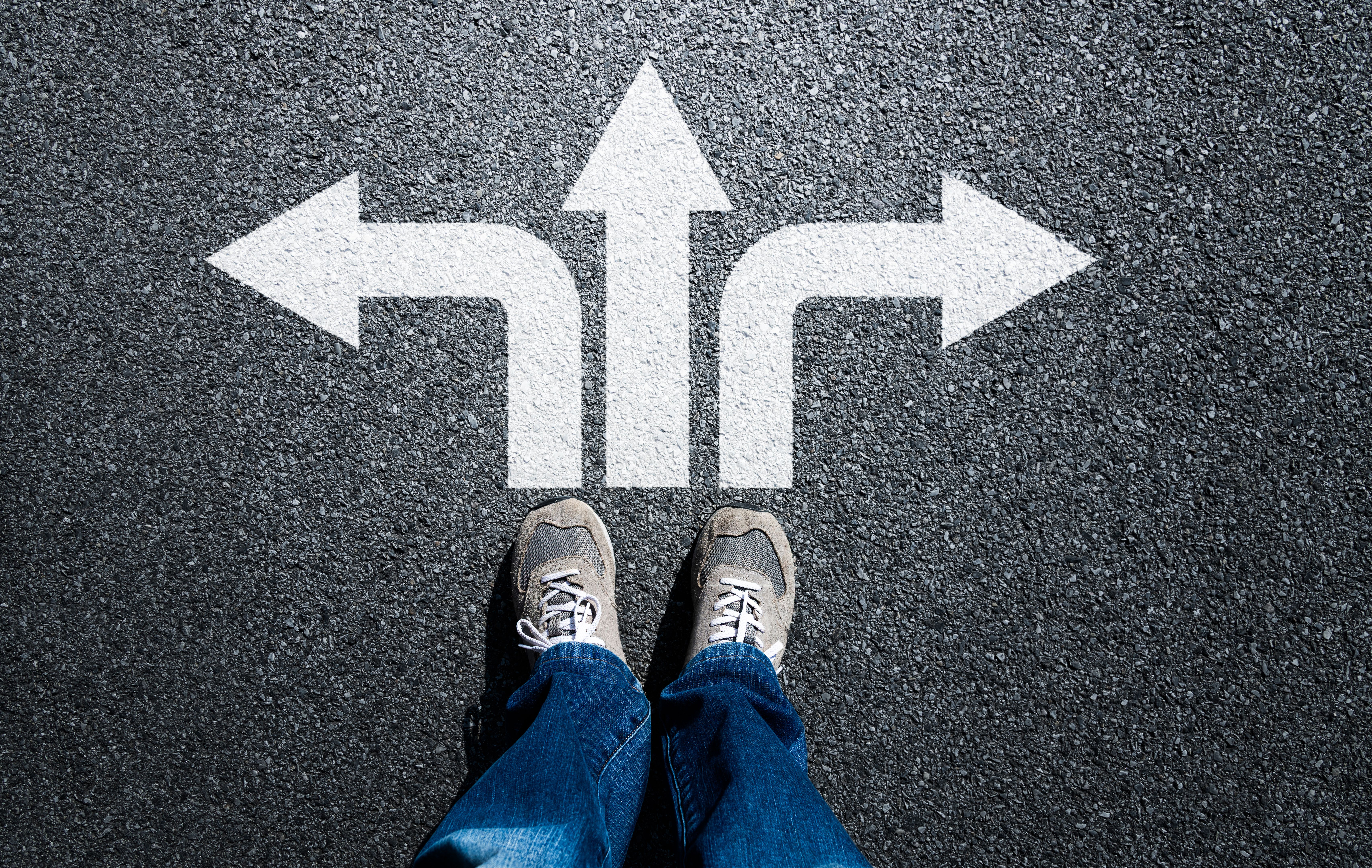 Top view of unrecognizable man standing in front of three arrow signs showing different ways choice