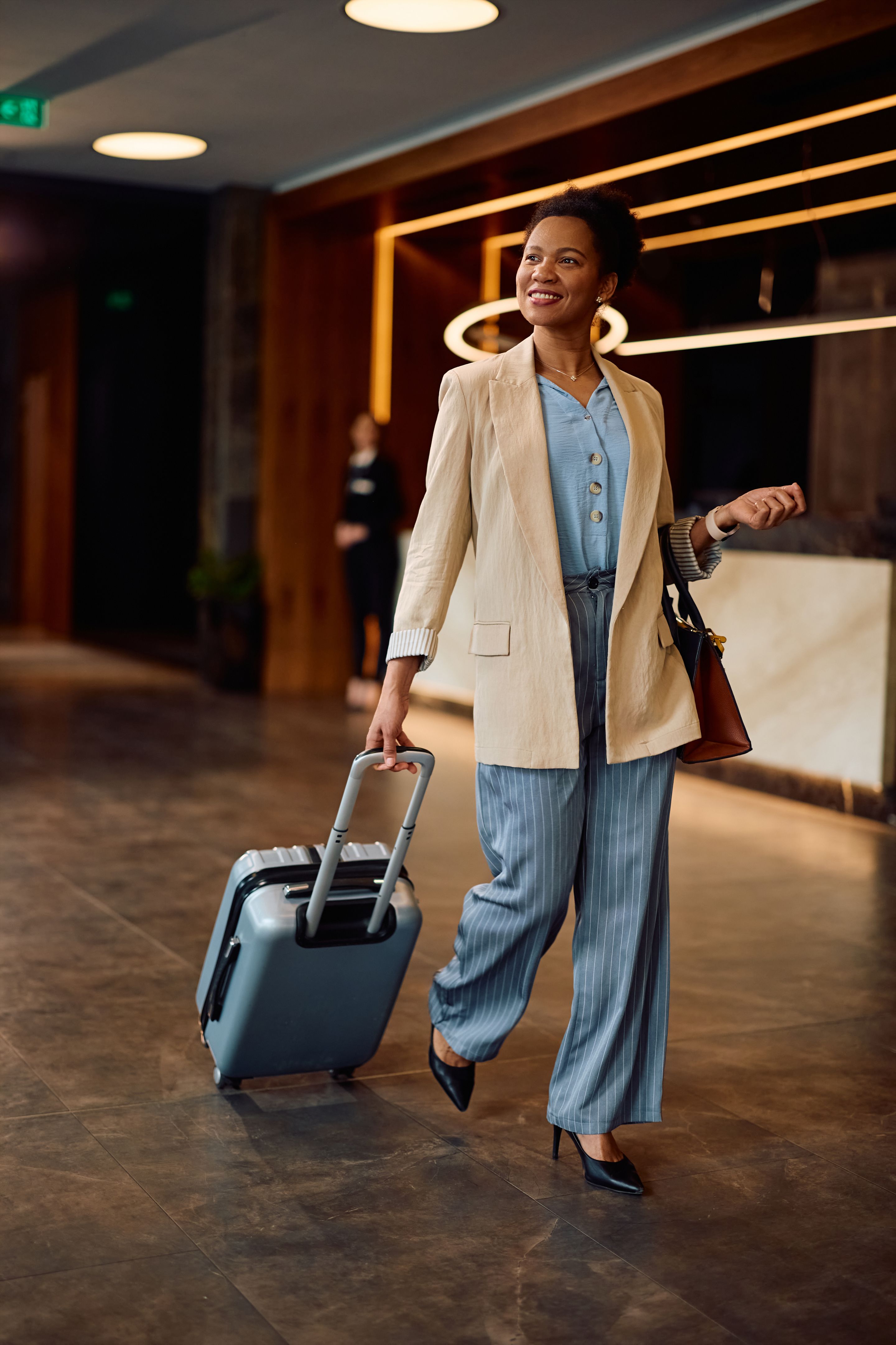 Happy black businesswoman with suitcase arriving at the hotel.