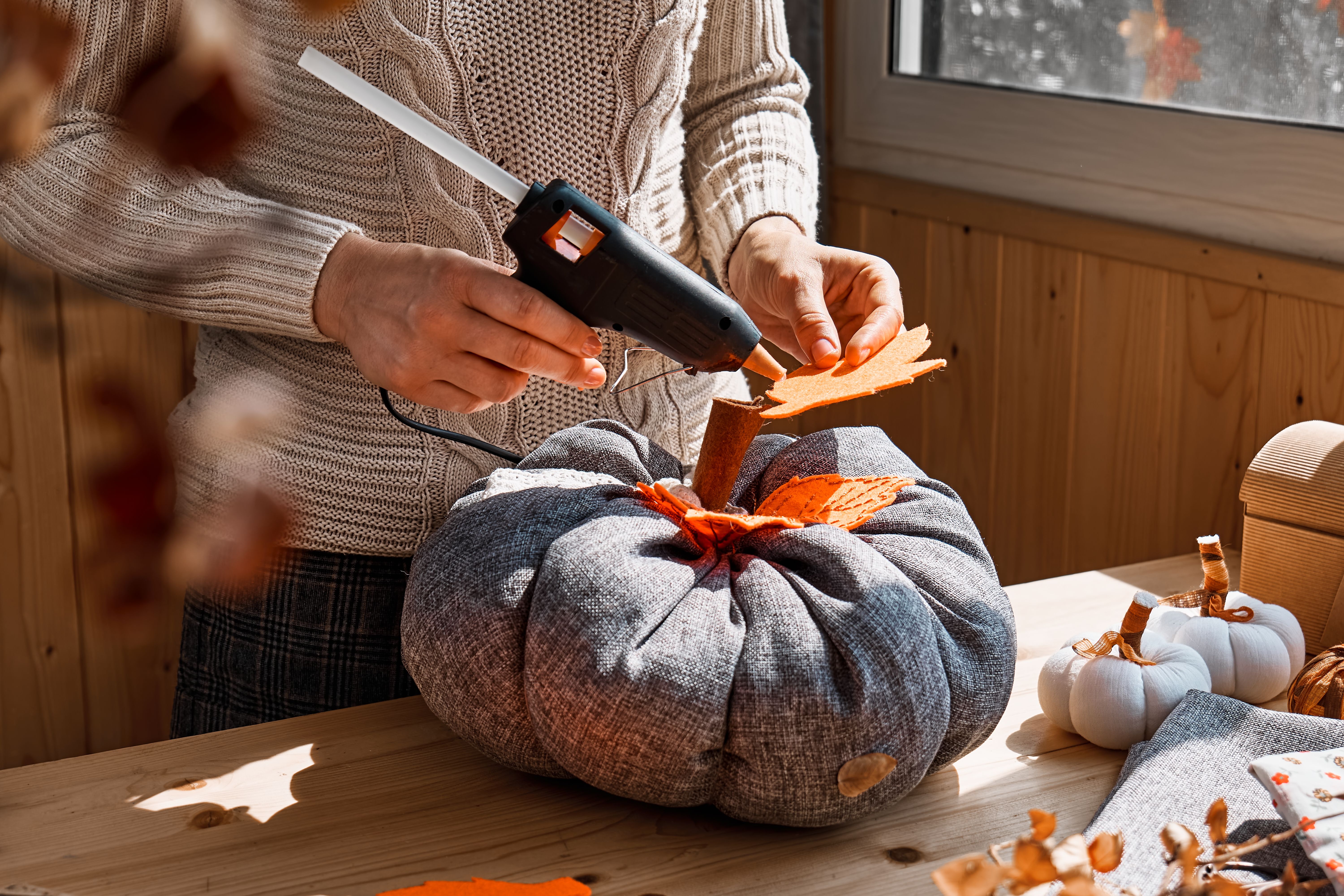 Cozy pumpkins. Woman making colorful fabric pumpkins. Autumn decoration with handmade textile pumpkin on wooden table. Fall vibes. Thanksgiving decor.