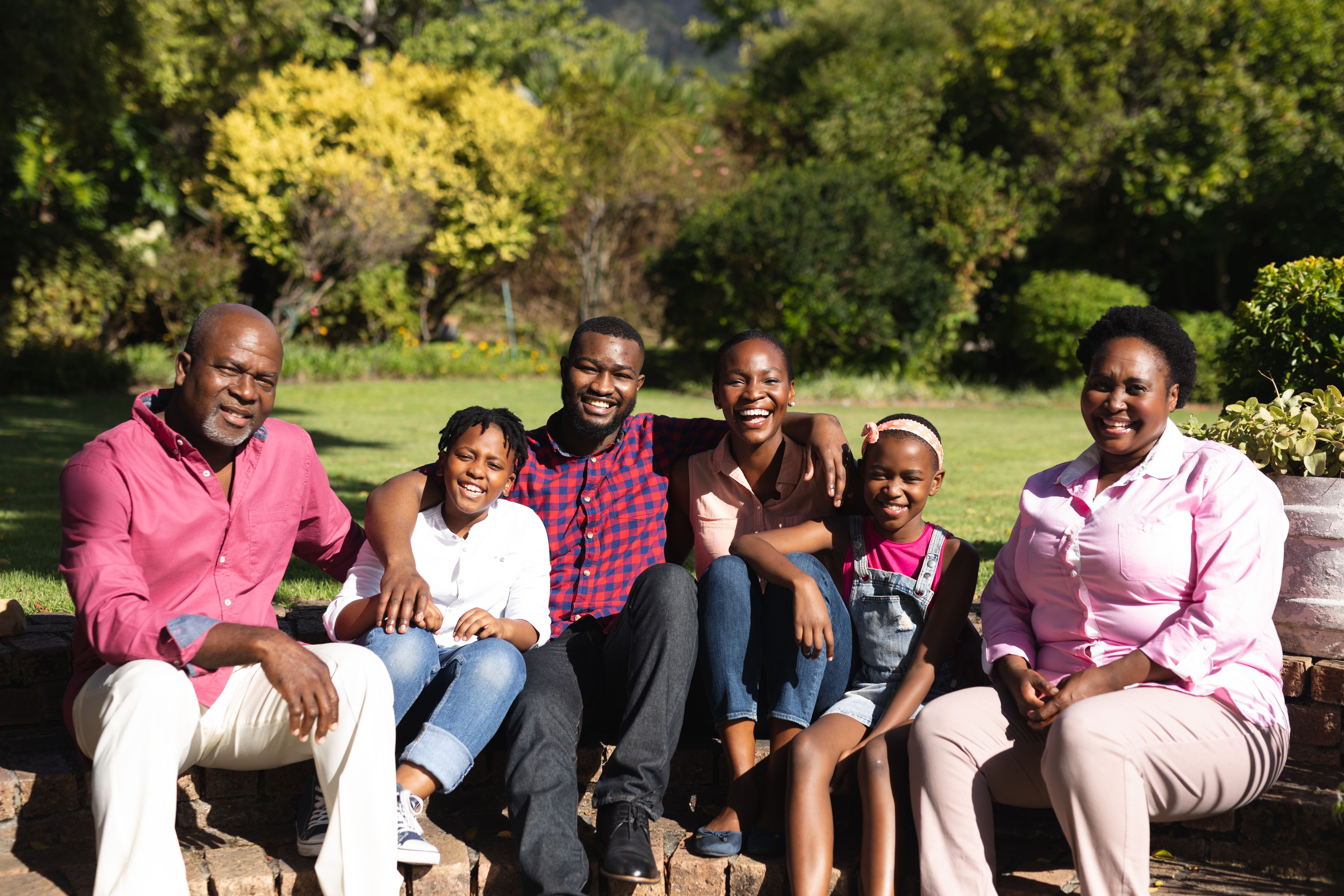 Smiling african american parents with children and their grandparents sitting embracing outdoors