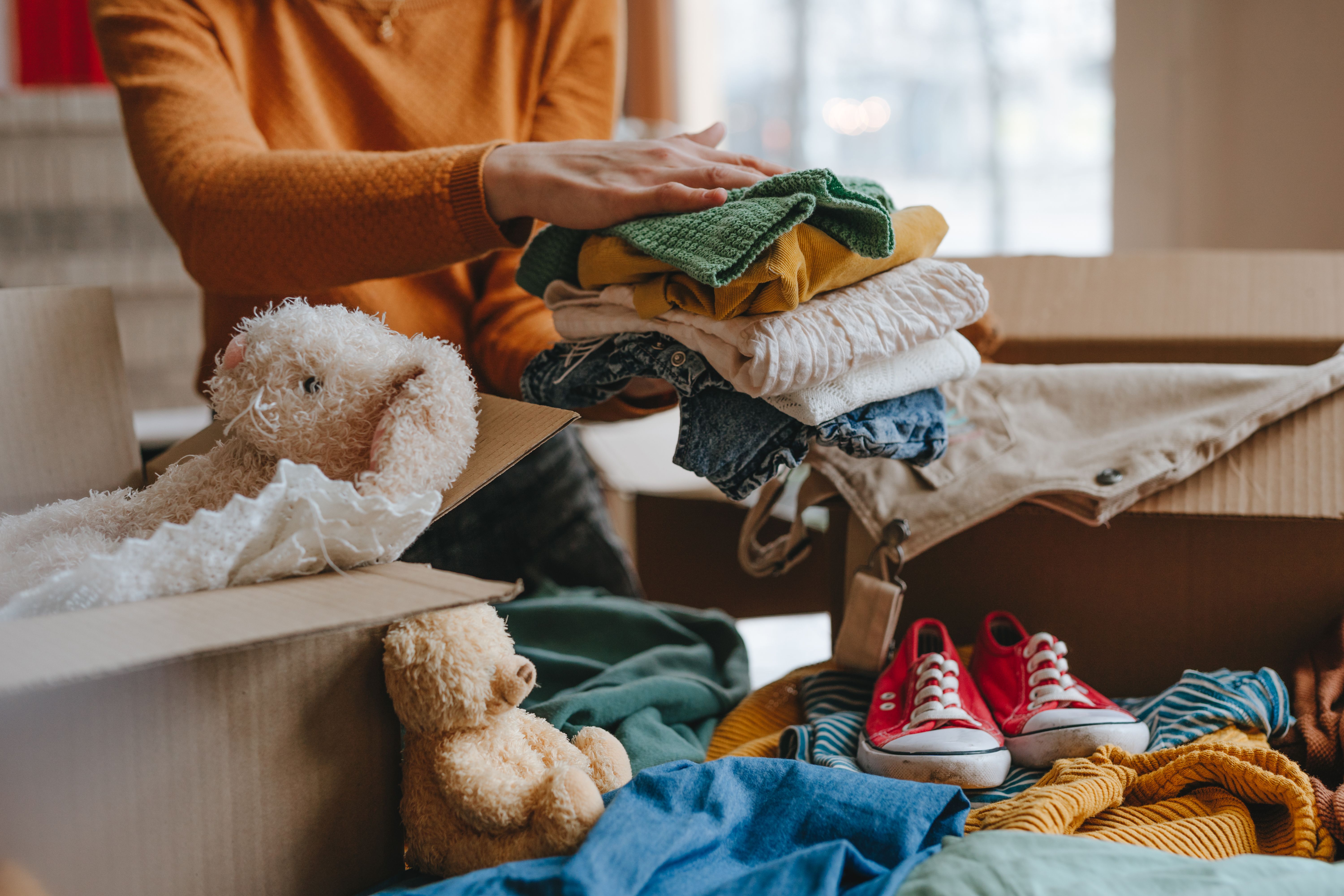 Woman sorting an old out-of-use kid toy, clothes and shoes in box for charity or upcycling Woman sorting an old out-of-use kid toy, clothes and shoes in box for charity or upcycling