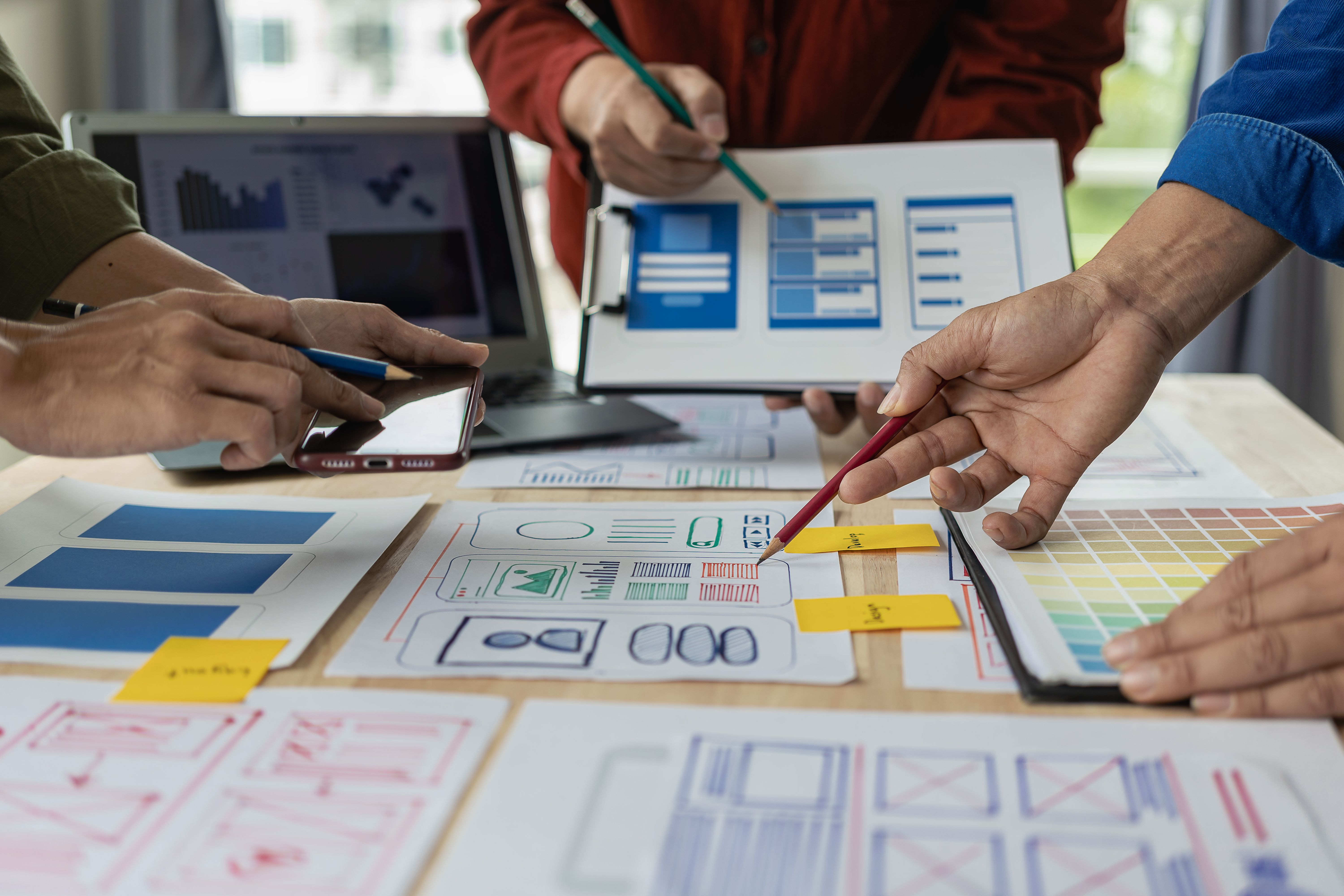 A team of web designers are working together to develop a mobile responsive website with UI/UX front end design concepts. A team of UxUi developers are working together at a wooden workbench.