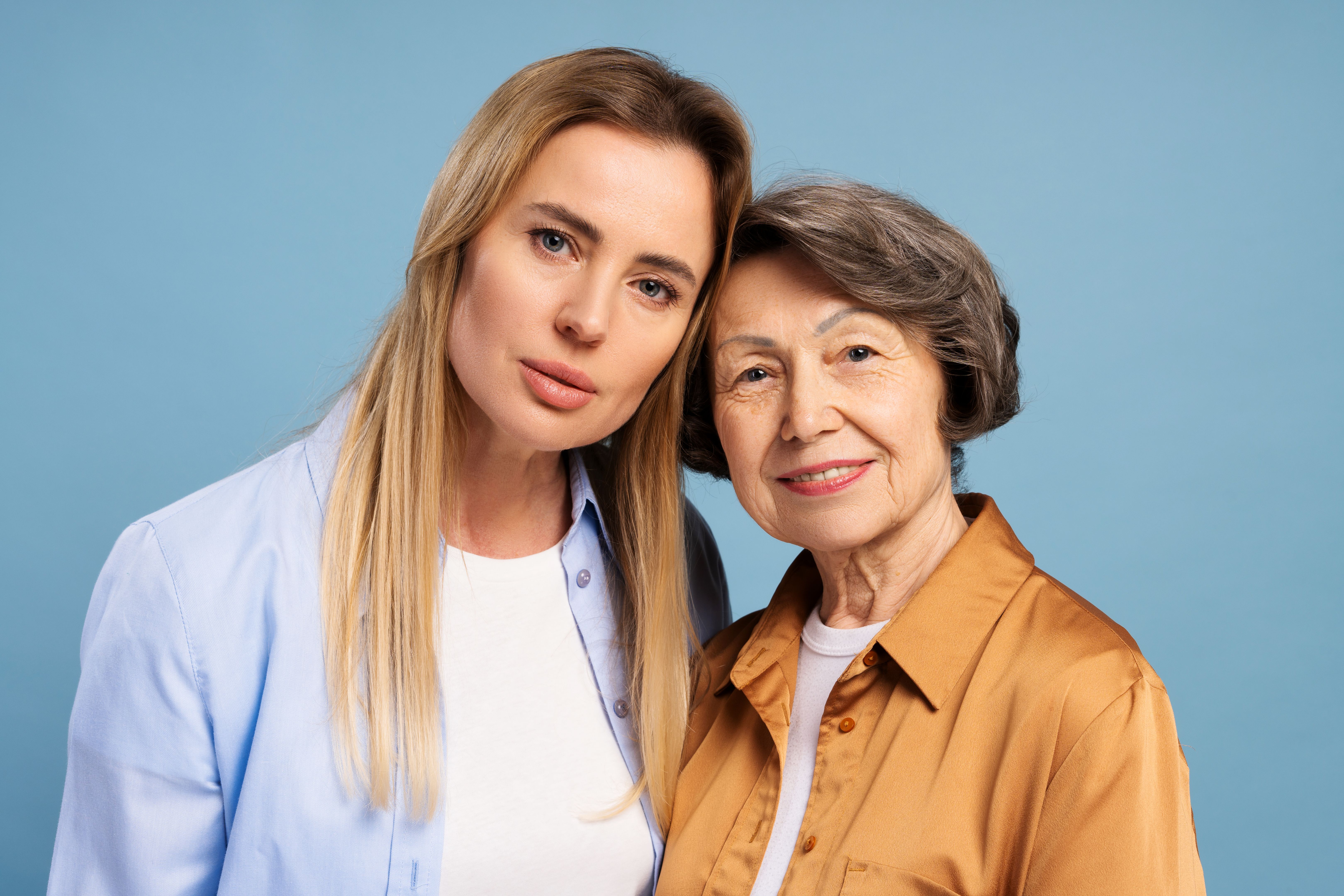 Happy senior mother and adult daughter posing together on blue background