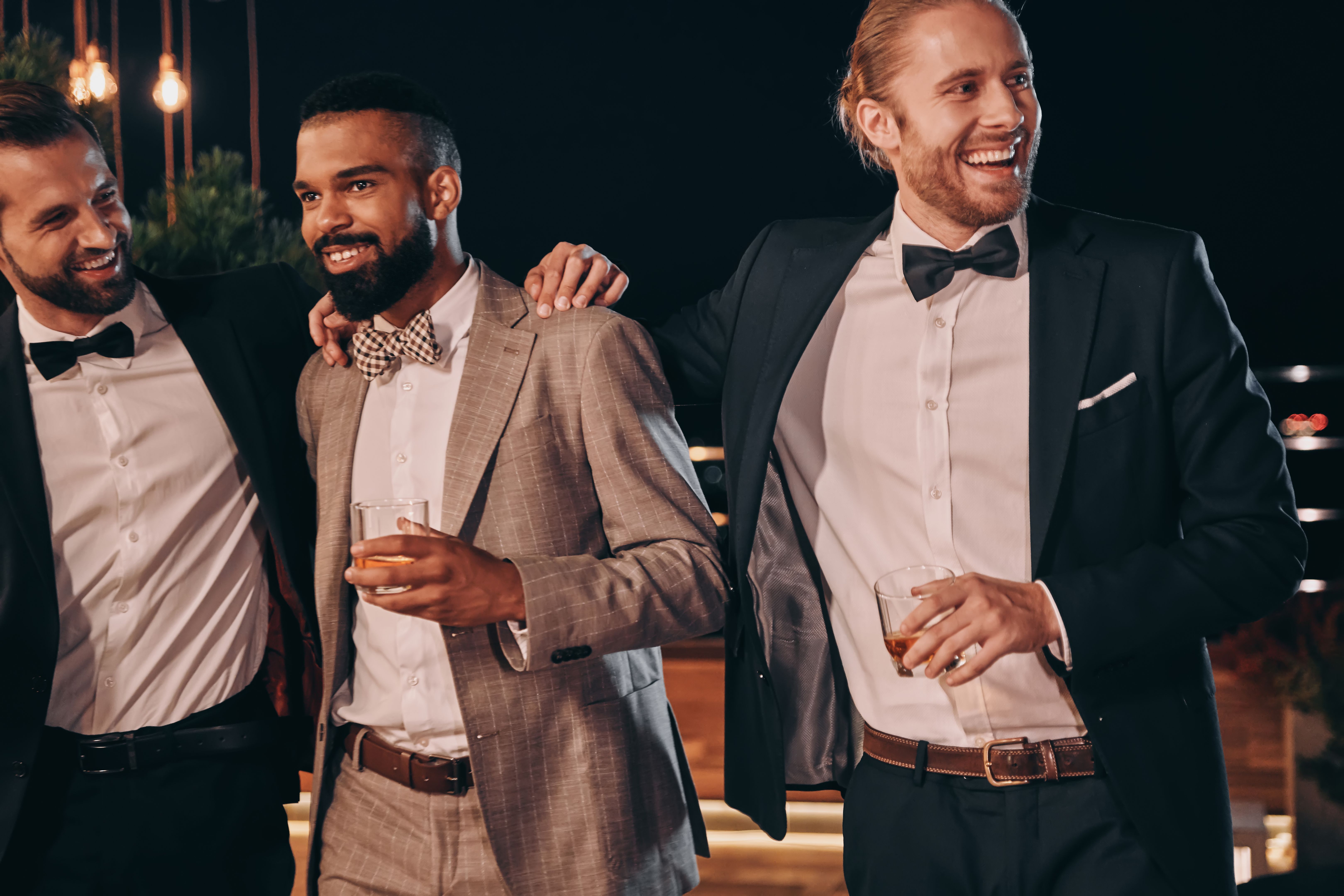Three handsome men in suits bonding and drinking whiskey