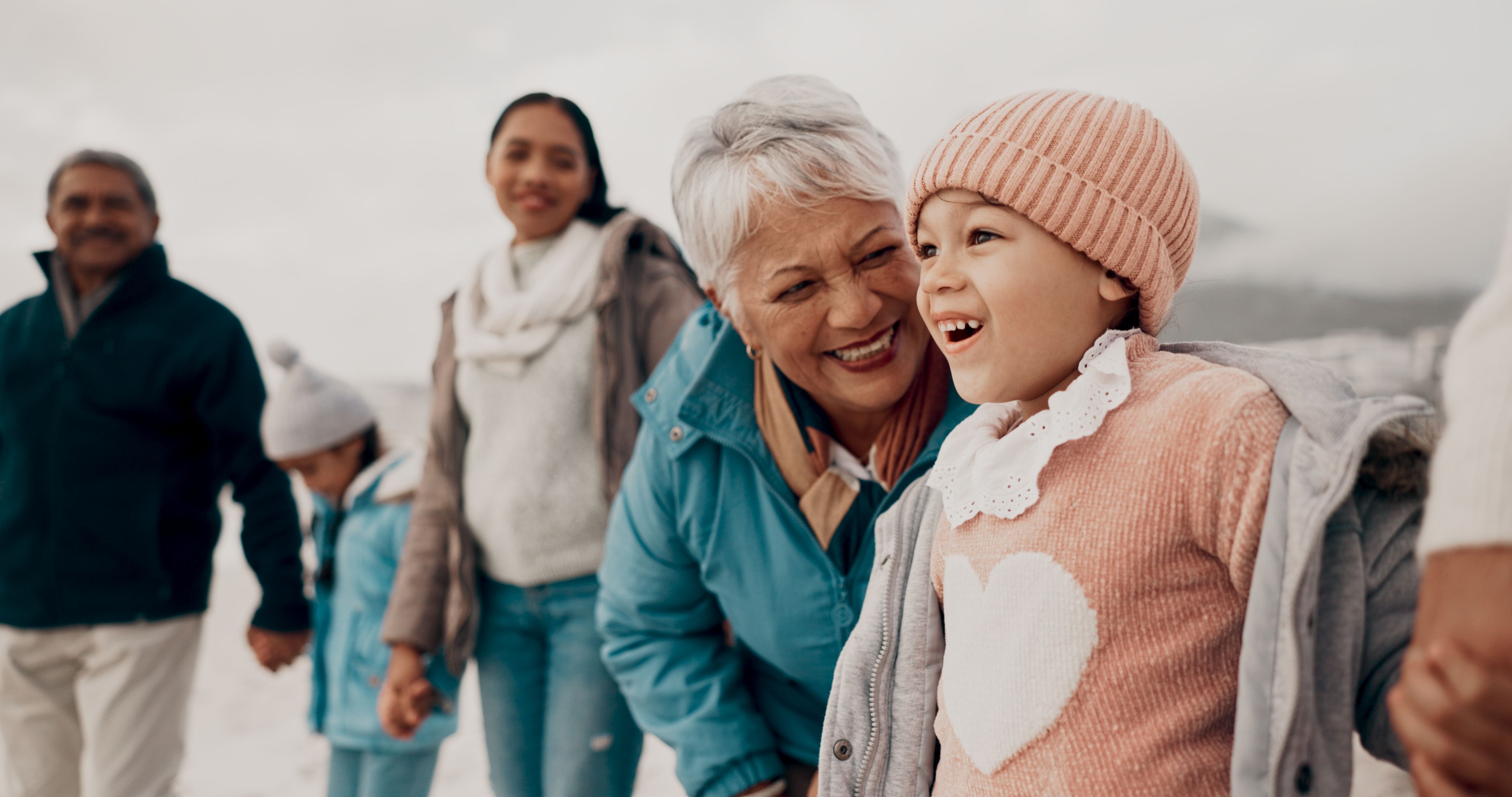 Grandmother, girl and family at beach with smile, holding hands or outdoor with care, walk and vacation. People, generations and kids with laugh for funny conversation with bonding on winter holiday