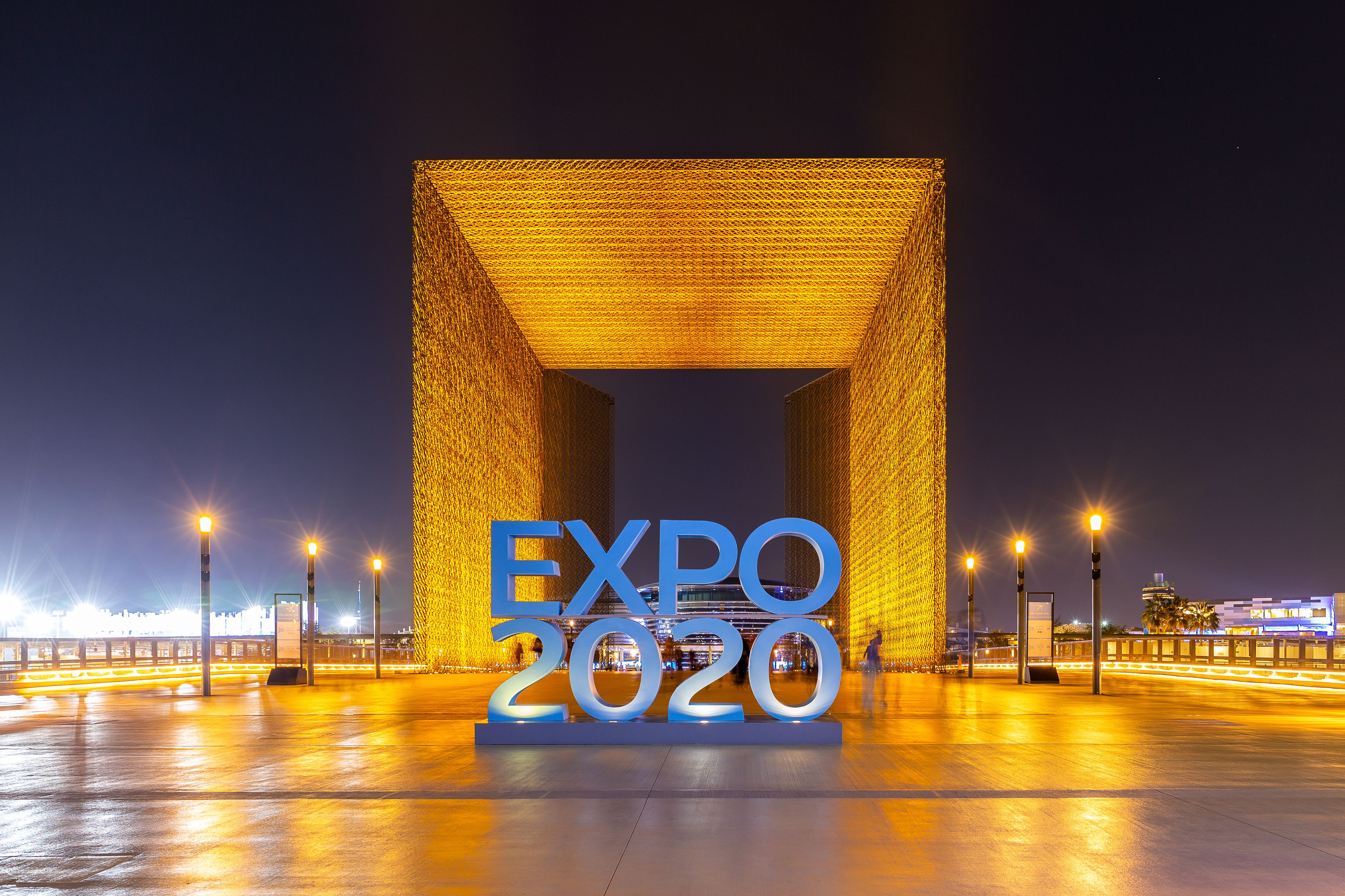 Expo 2020 Dubai blue logo sign with illuminated entrance gateway at night.