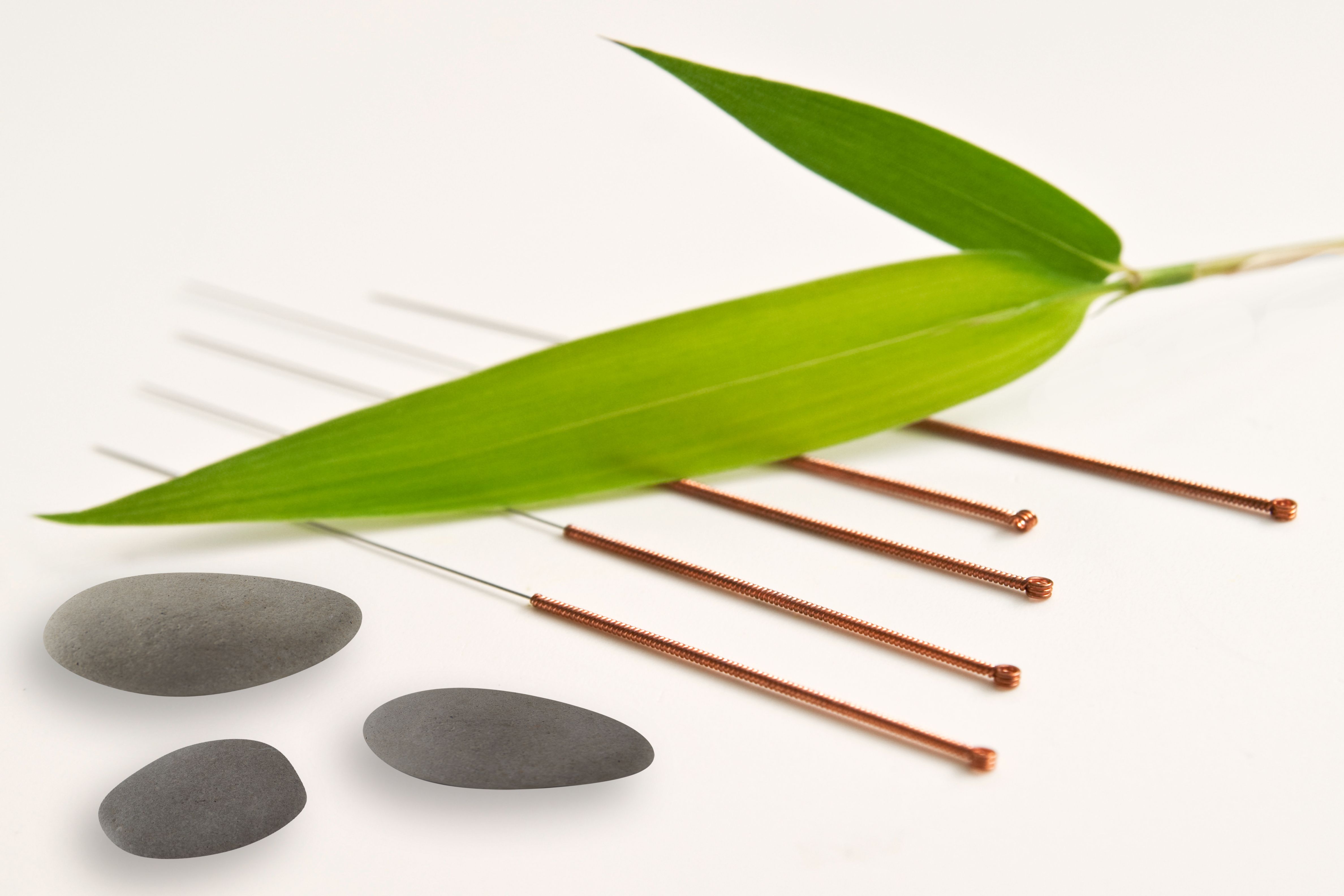 Acupuncture needles with bamboo leaf and stones background
