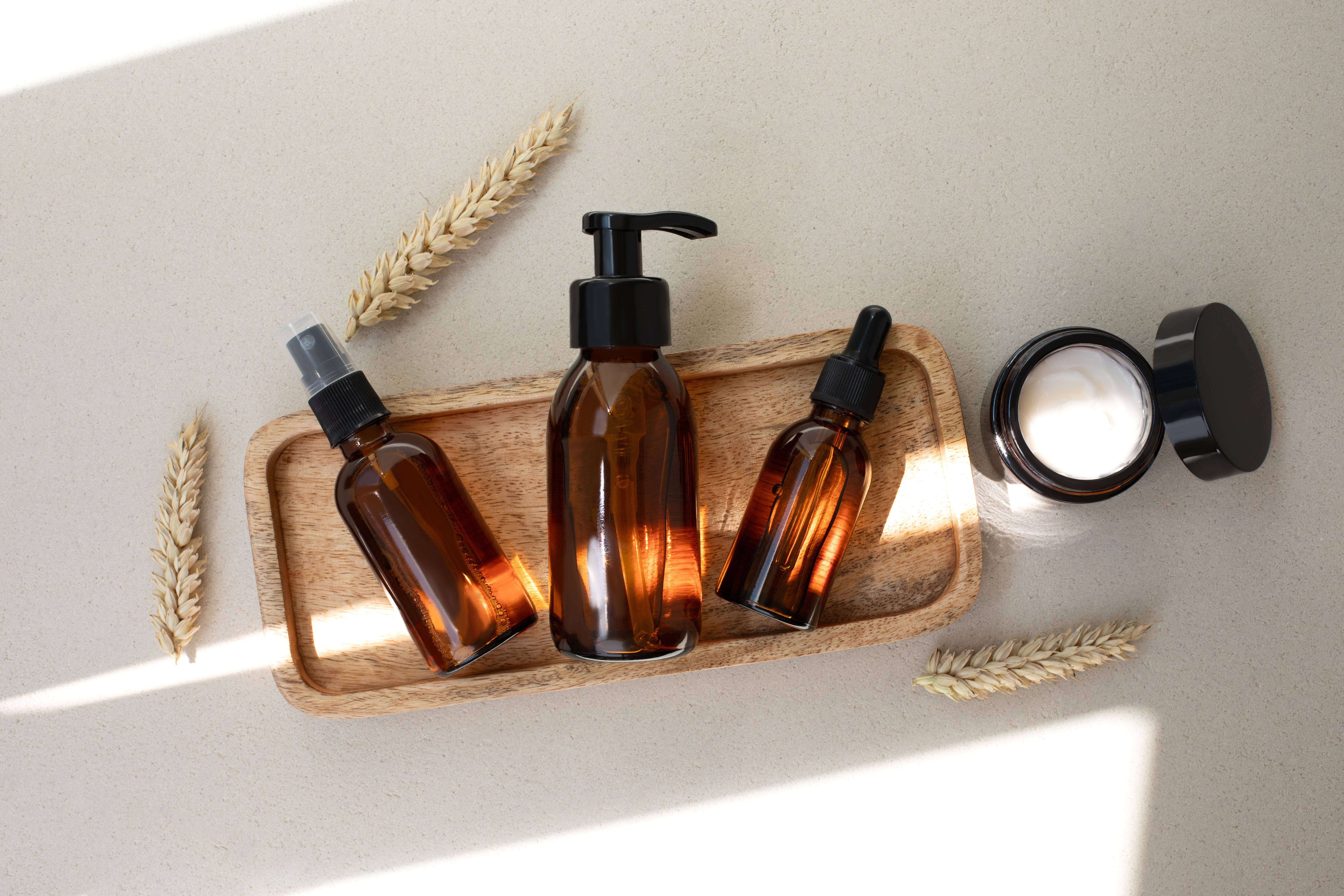 Amber bottles with facial cosmetics on a wooden tray on the beige concrete background Amber bottles with facial cosmetics on a wooden tray on the beige concrete background