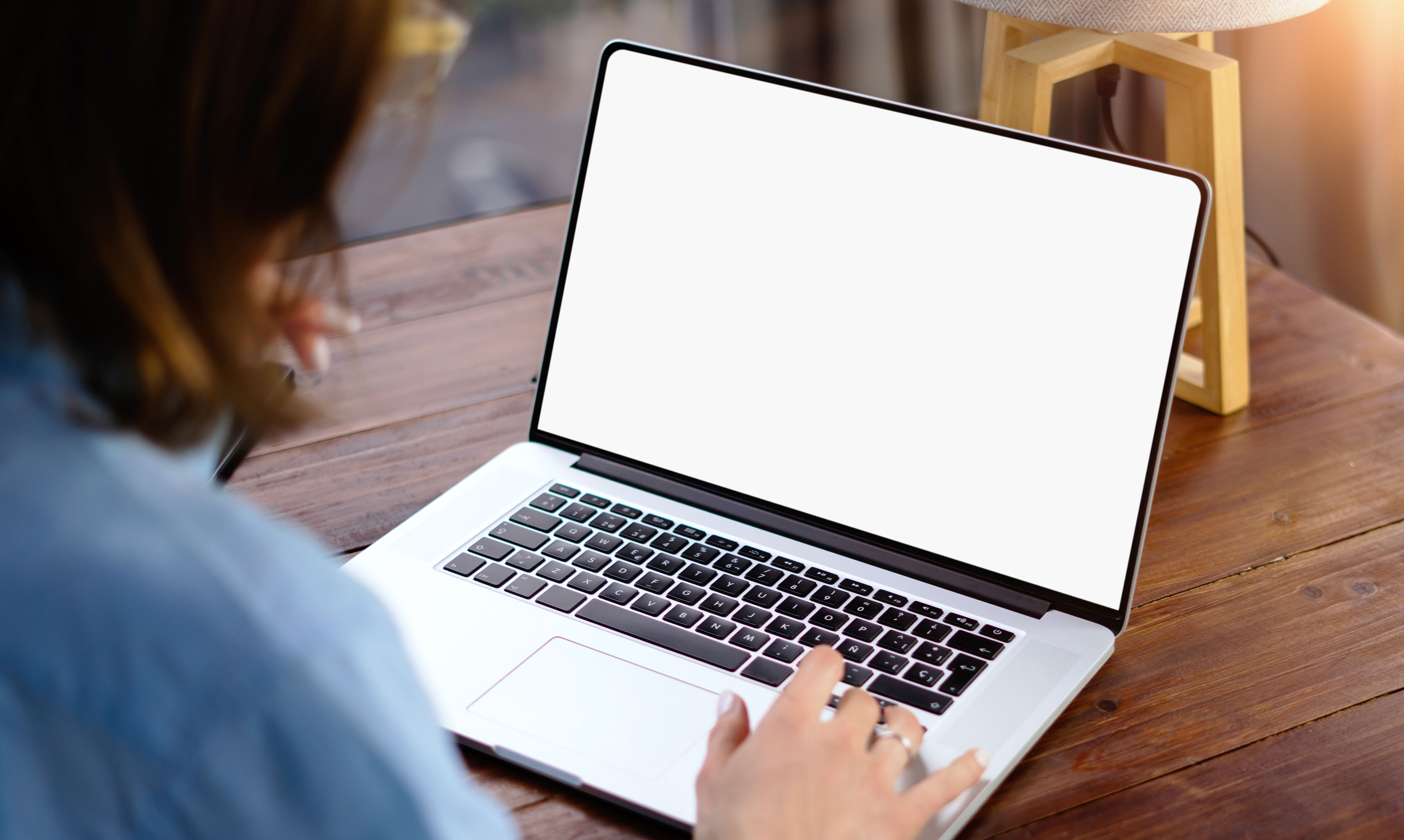 Mockup image of a woman using laptop with blank screen on wooden table