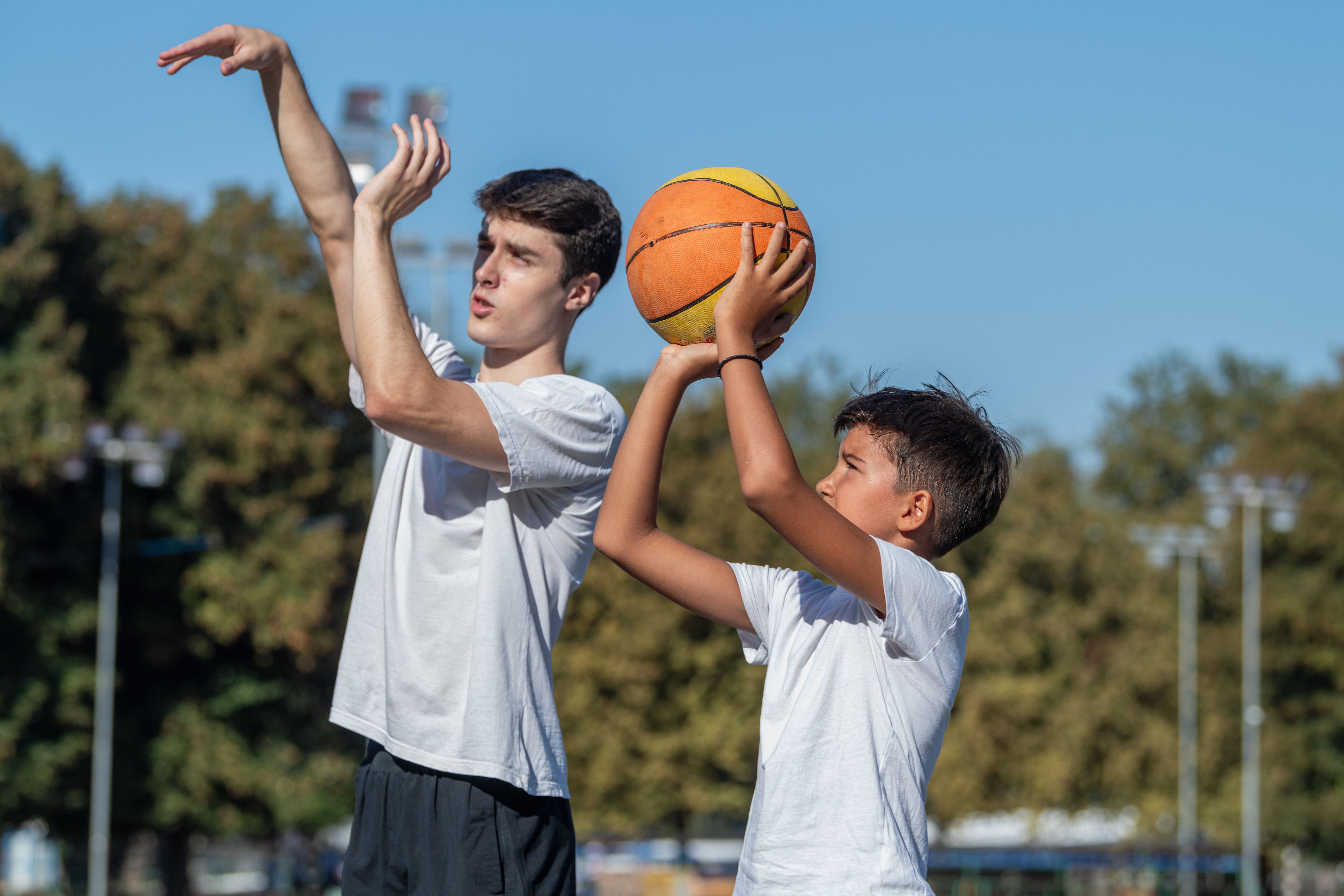 Outdoor basketball training for kids, featuring a coach teaching a young boy shooting technique. Focus on skill building, precision, and fostering youth development in sports.
