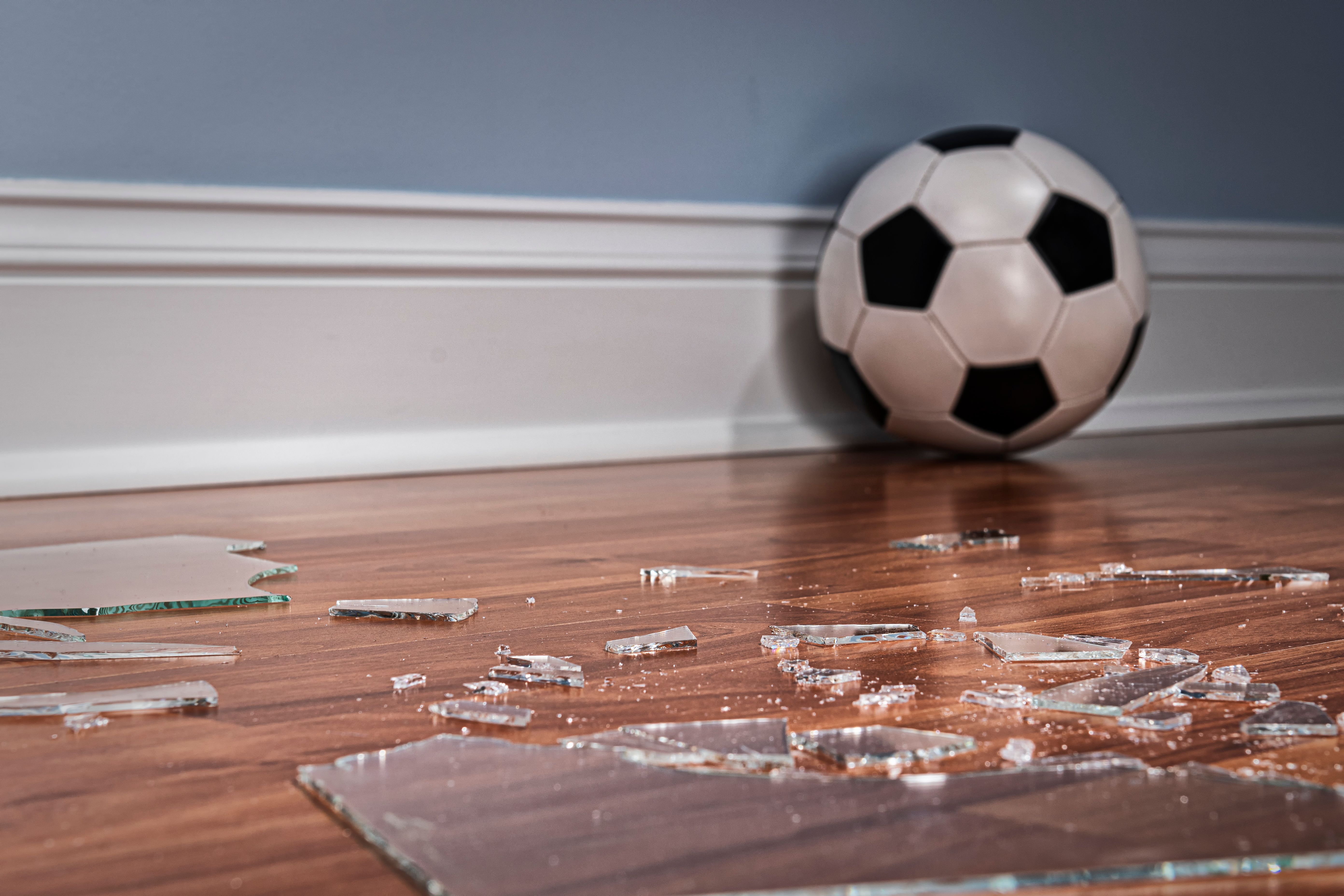 Verre cassé d'une vitre sur le plancher avec le ballon de football