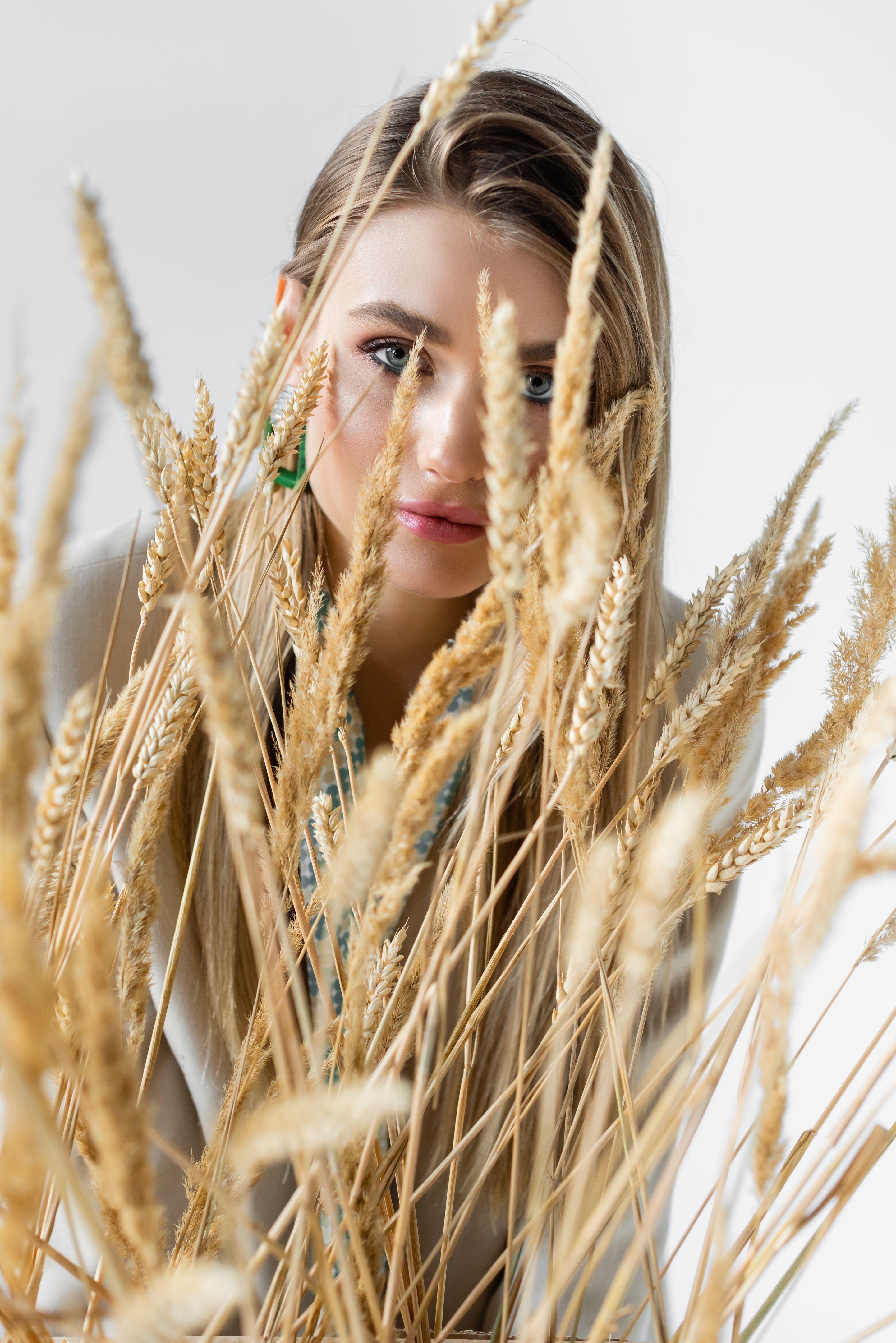 young woman looking at camera through spikelets of wheat on blurred foreground