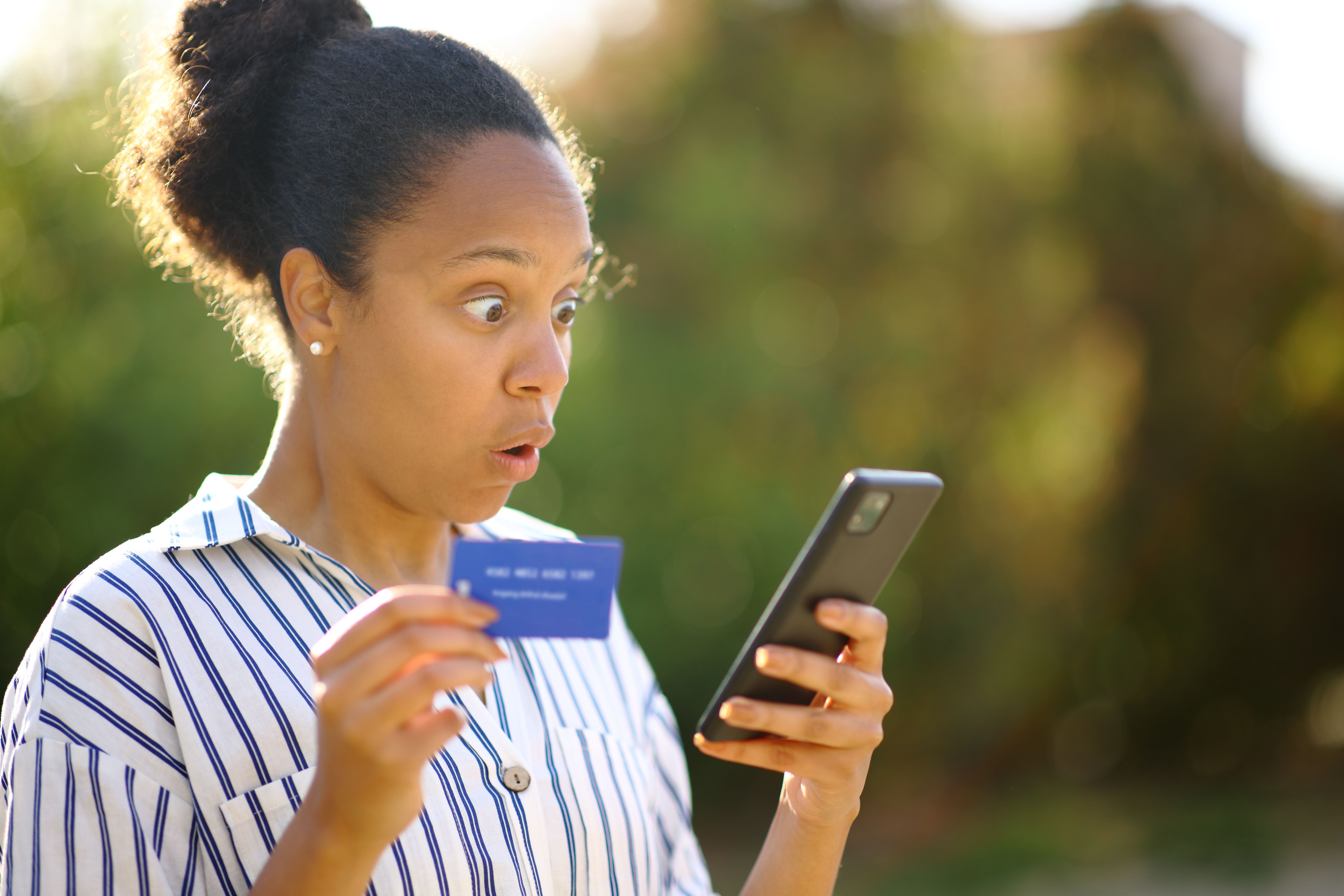 Surprised black buyer using phone and credit card Surprised black buyer using phone and credit card