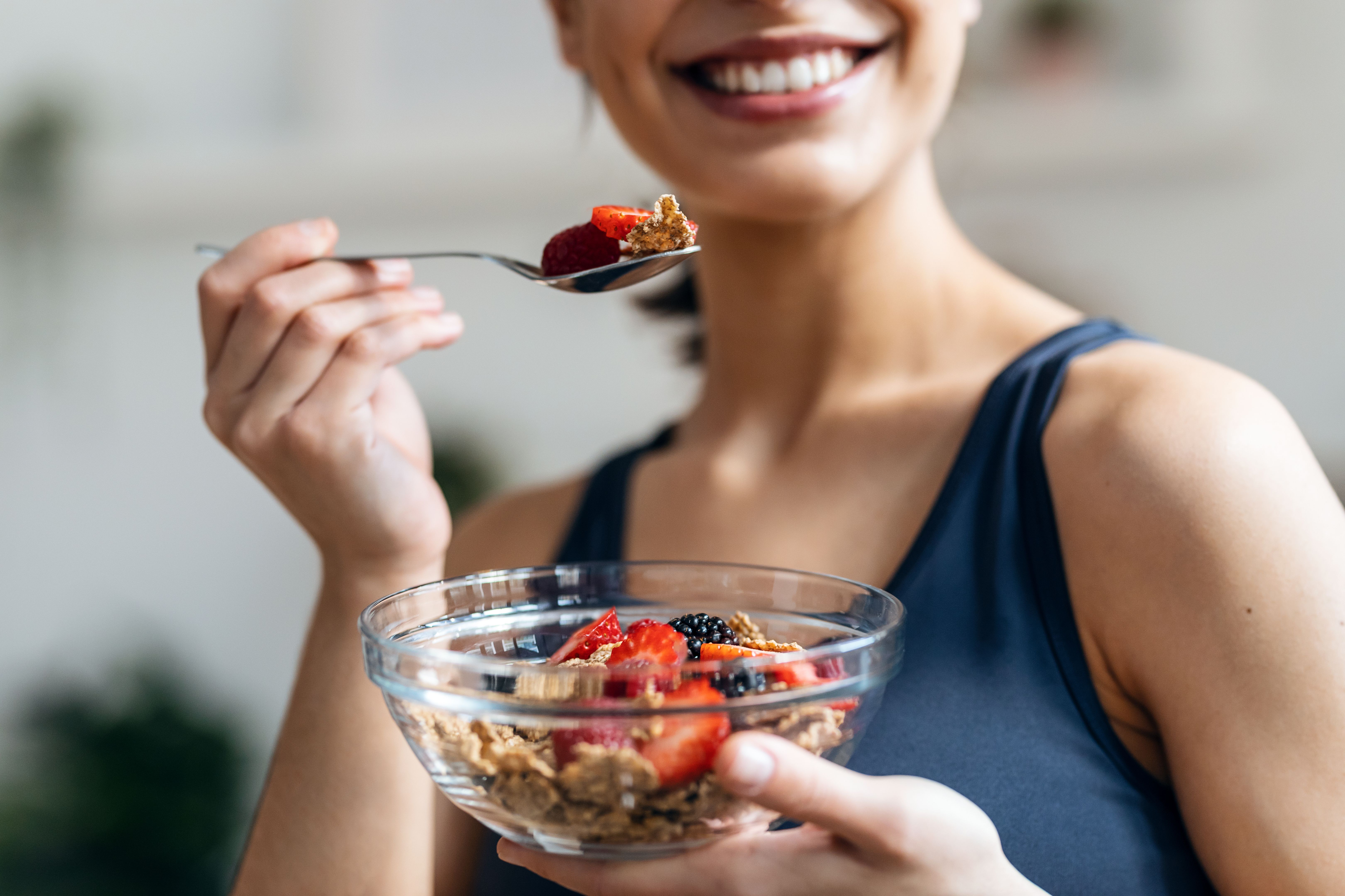 Athletic woman eating a healthy bowl of muesli with fruit in the kitchen at home Athletic woman eating a healthy bowl of muesli with fruit in the kitchen at home