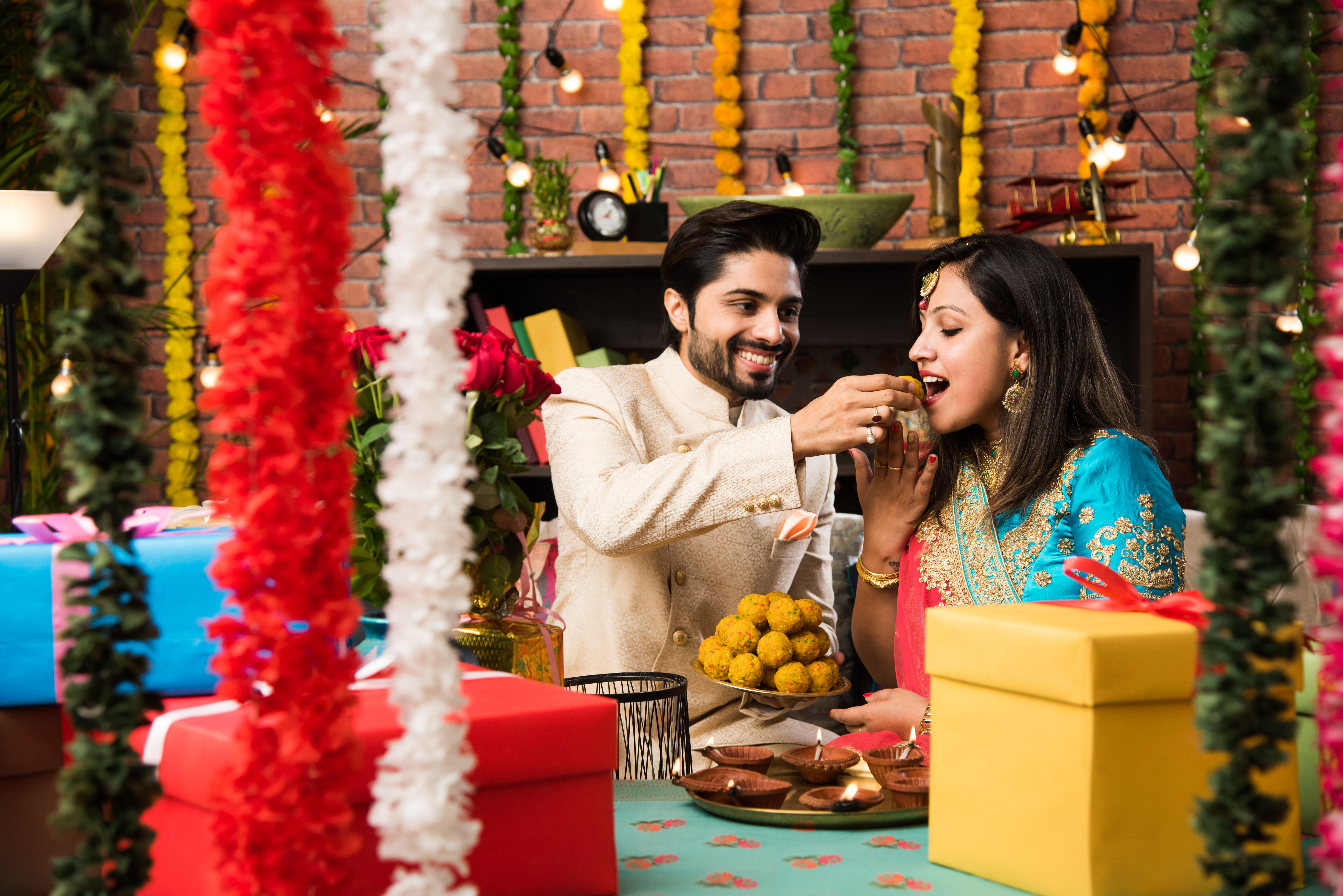 Indian smart couple eating sweet laddu on Diwali or anniversary, selective focus