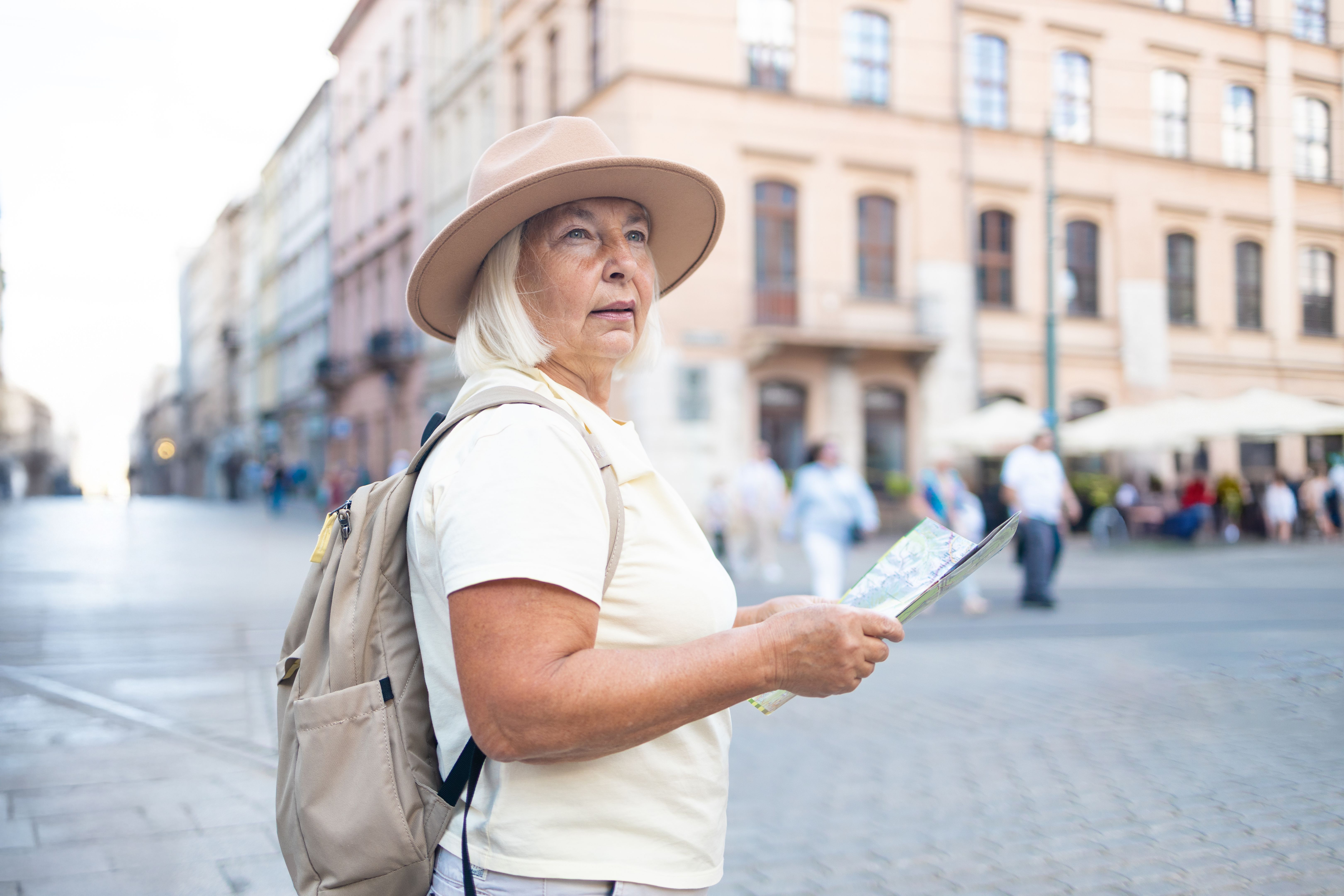 Senior woman reading map in a city square, exploring travel destination.