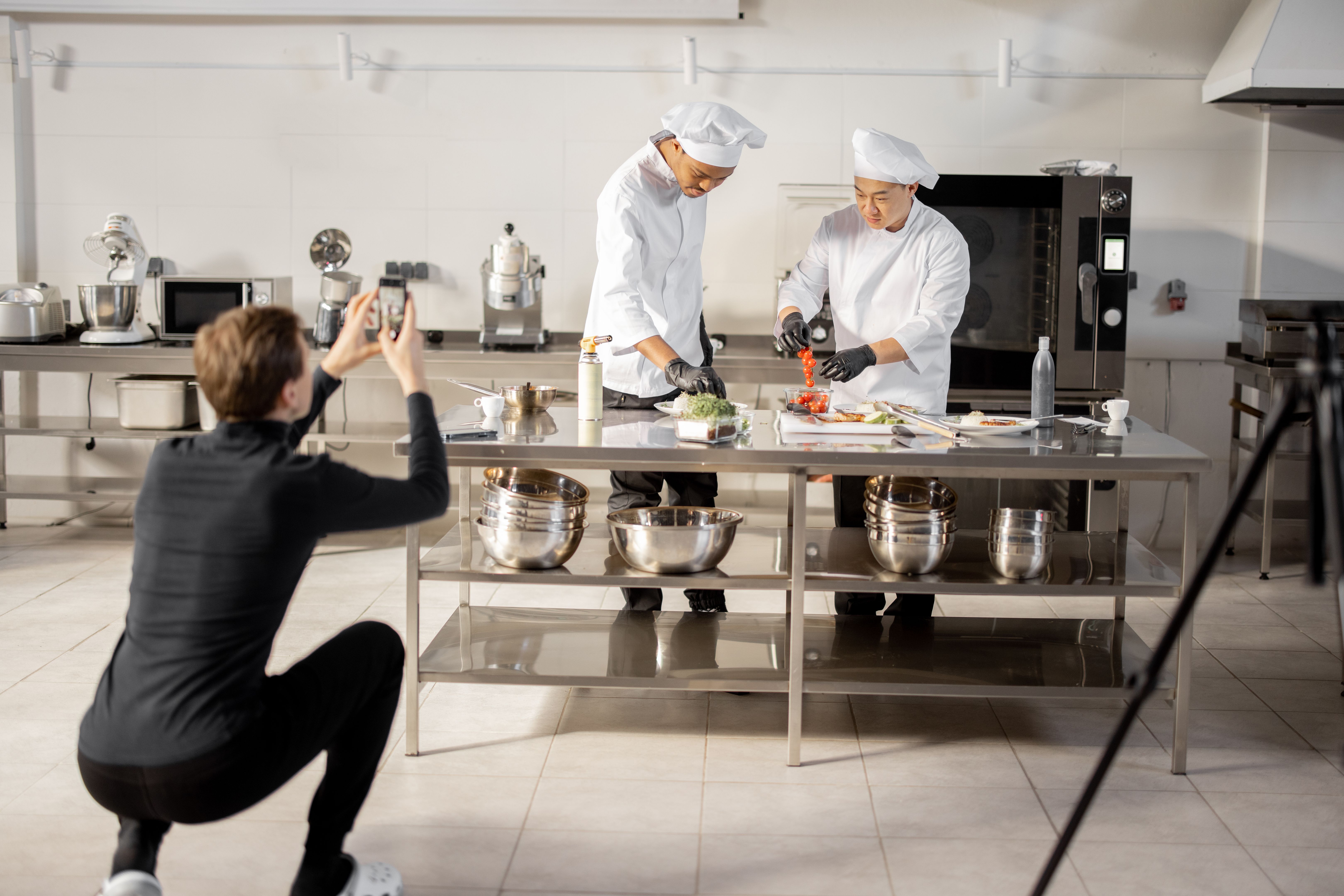 Man records on phone the process of cooking by two chefs in a professional kitchen