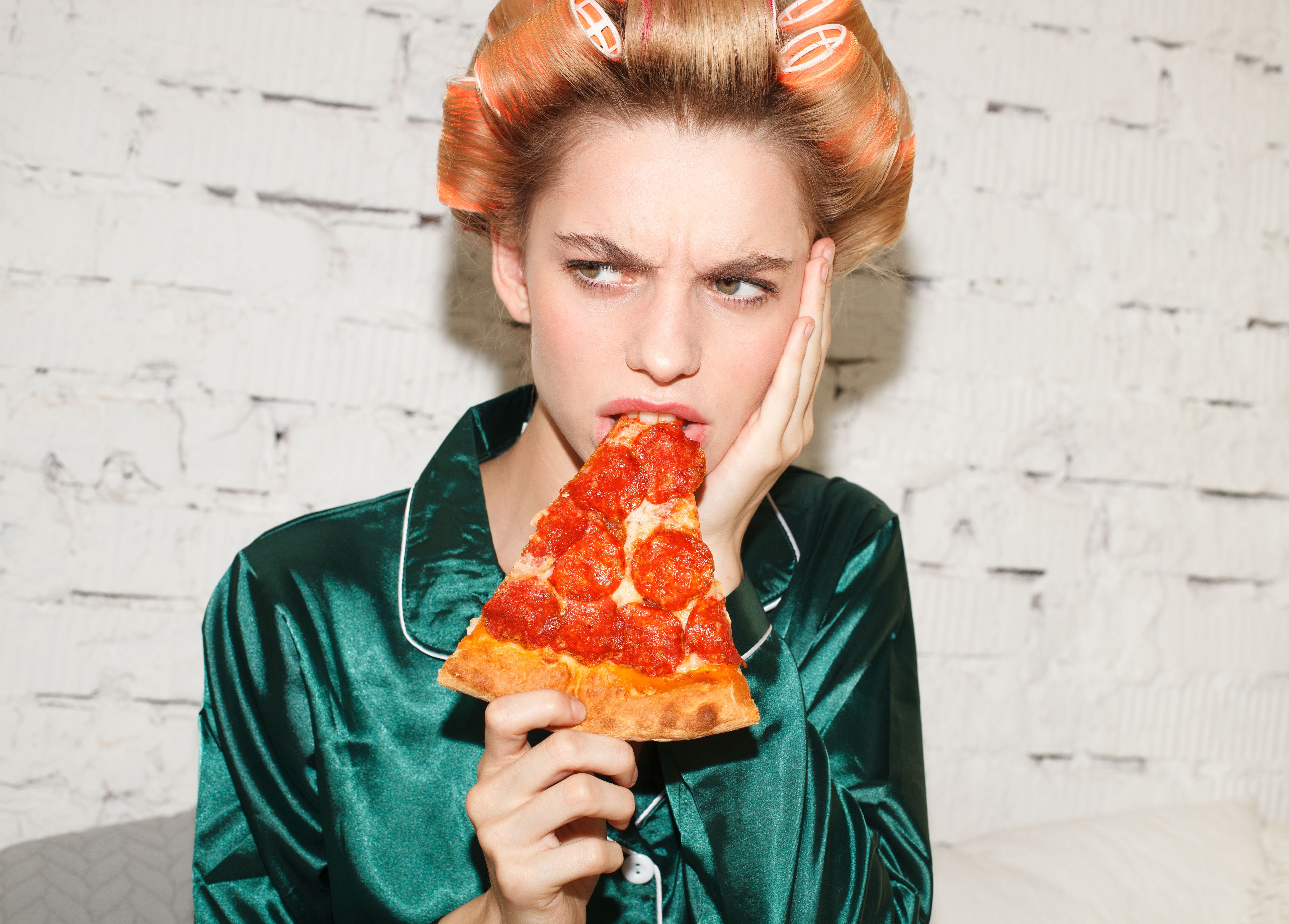 young ashamed female eating pizza in bed