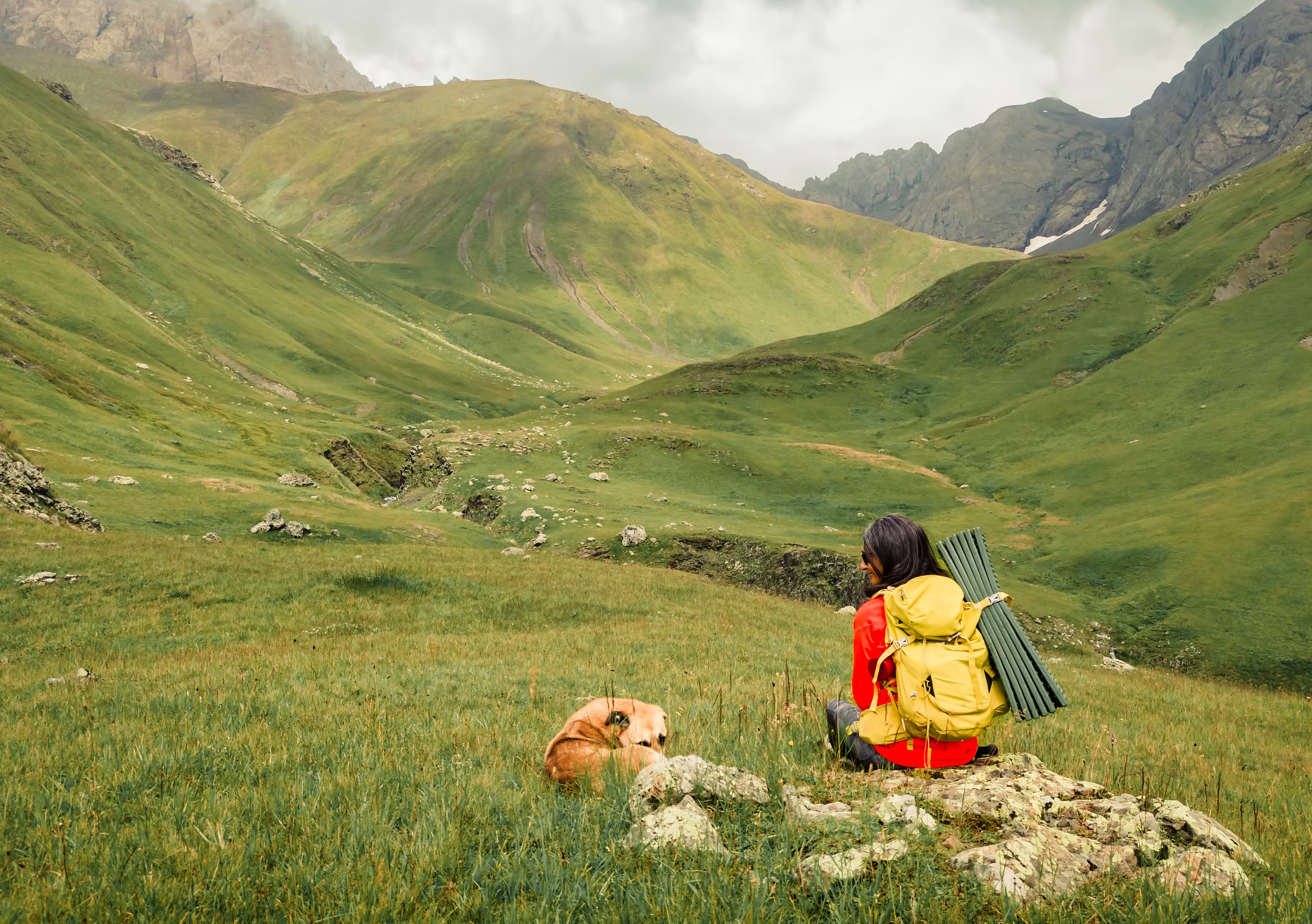 Young caucasian woman sit with her cute adult long haired adopted stray dog cuddle enjoying hike together in mountains. Man's best friend dog concept. Travel tourism with animal in autumn or fall