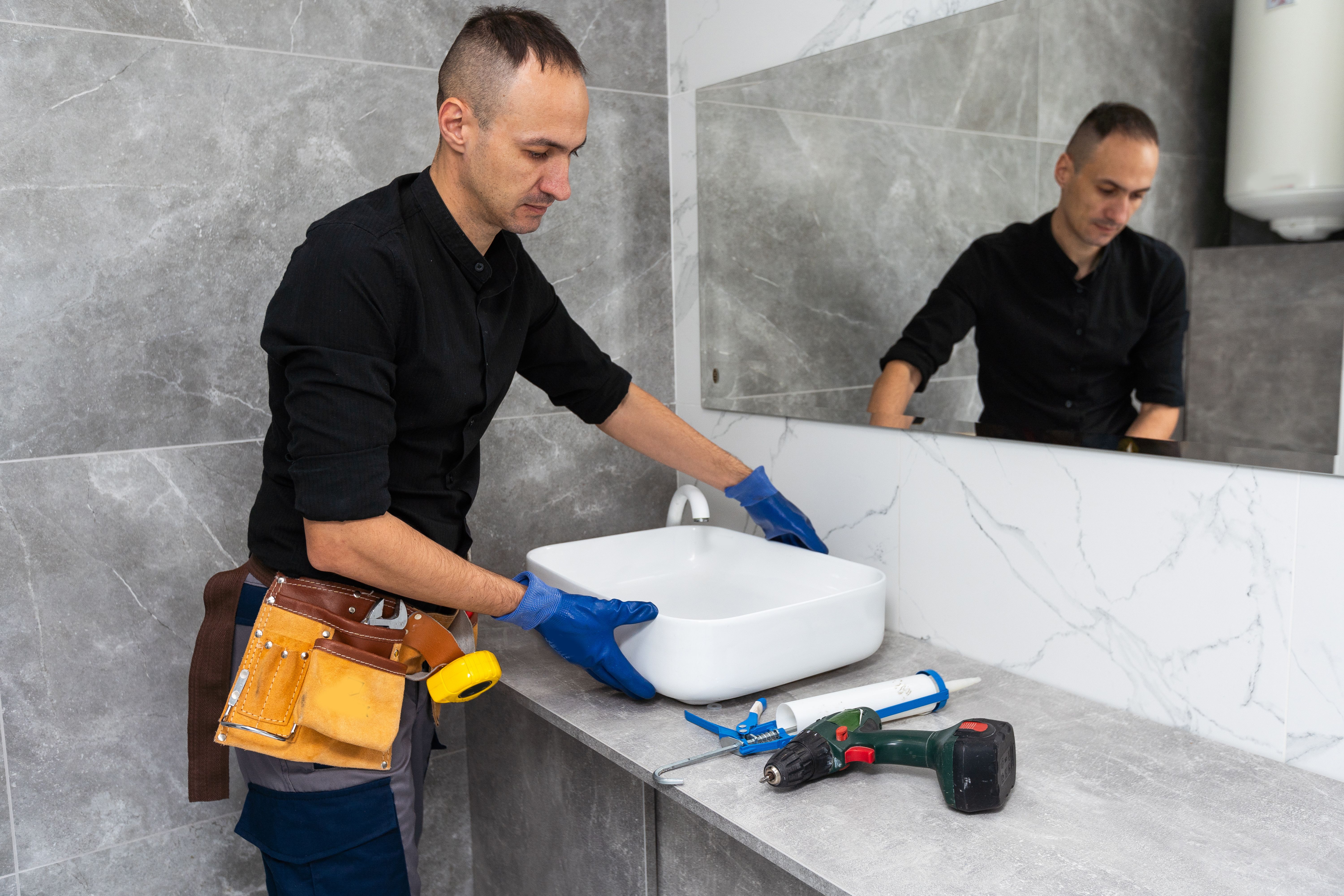 Professional plumber, male worker in uniform installing sink and water pipe in new apartment