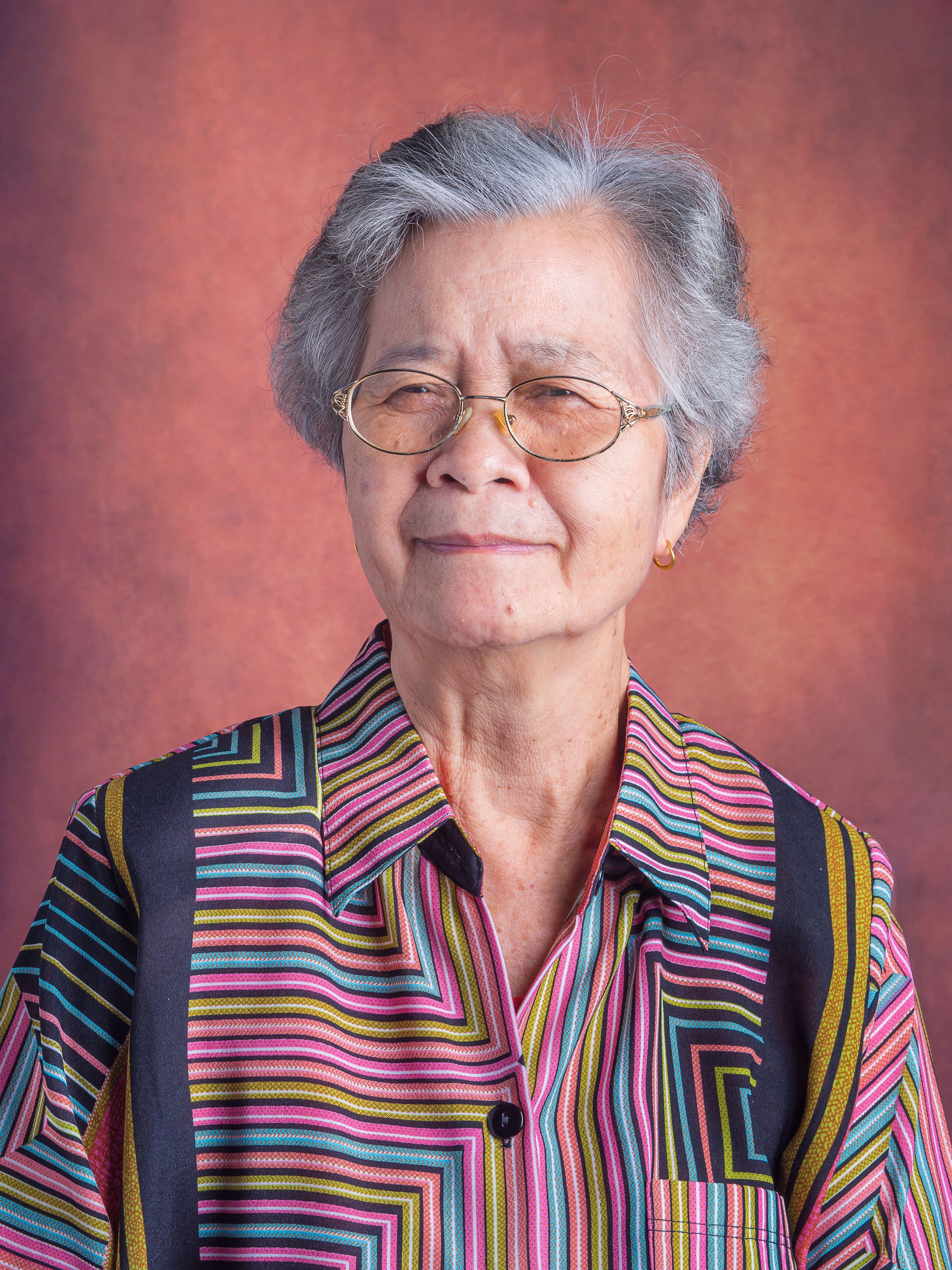 Portrait of a beautiful senior Asian woman wearing glasses with short white hair smiling and looking at the camera while standing with a vintage background