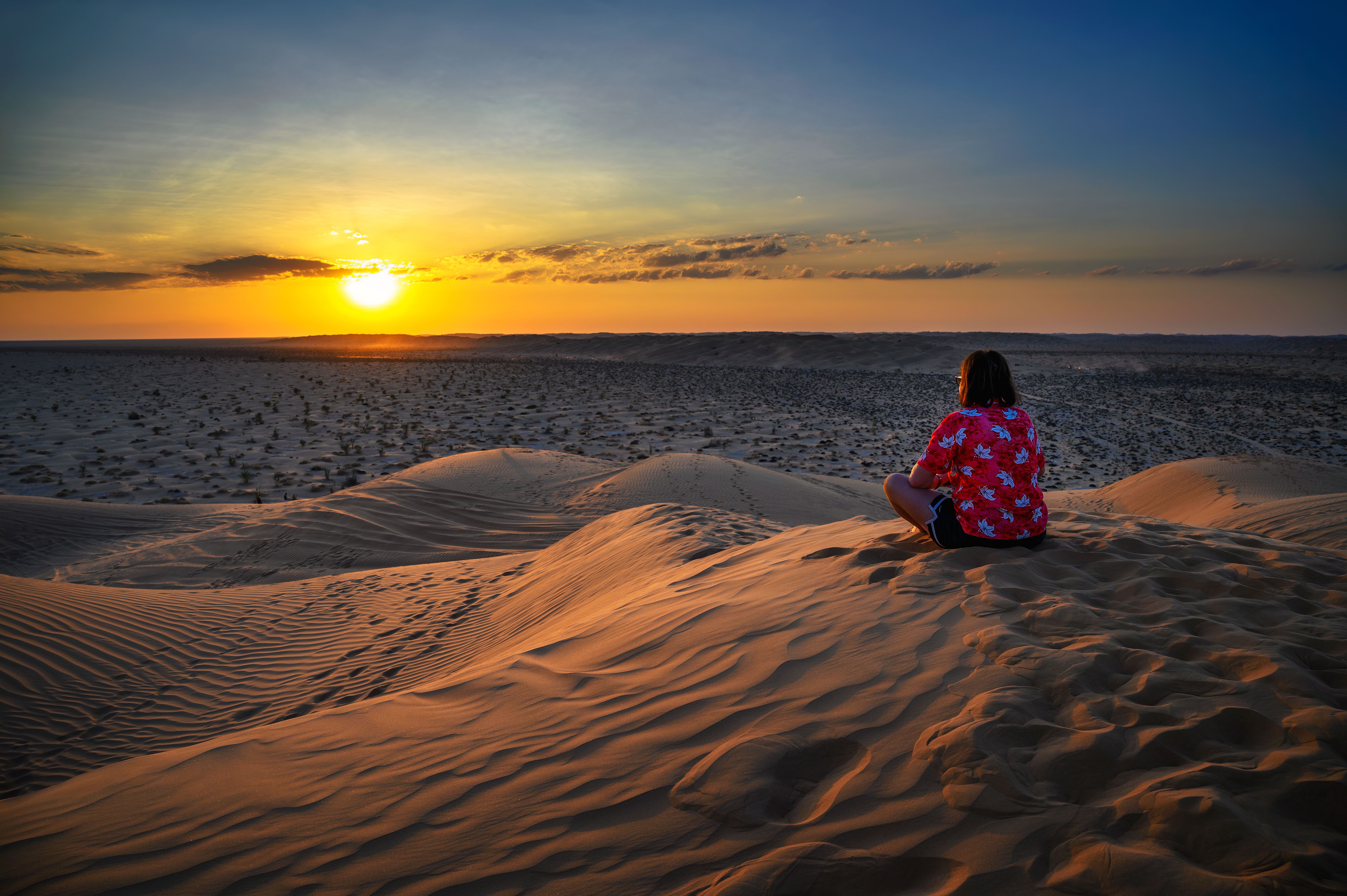 Woman watching a sunset over the sand dunes of the Arabian Desert in Oman