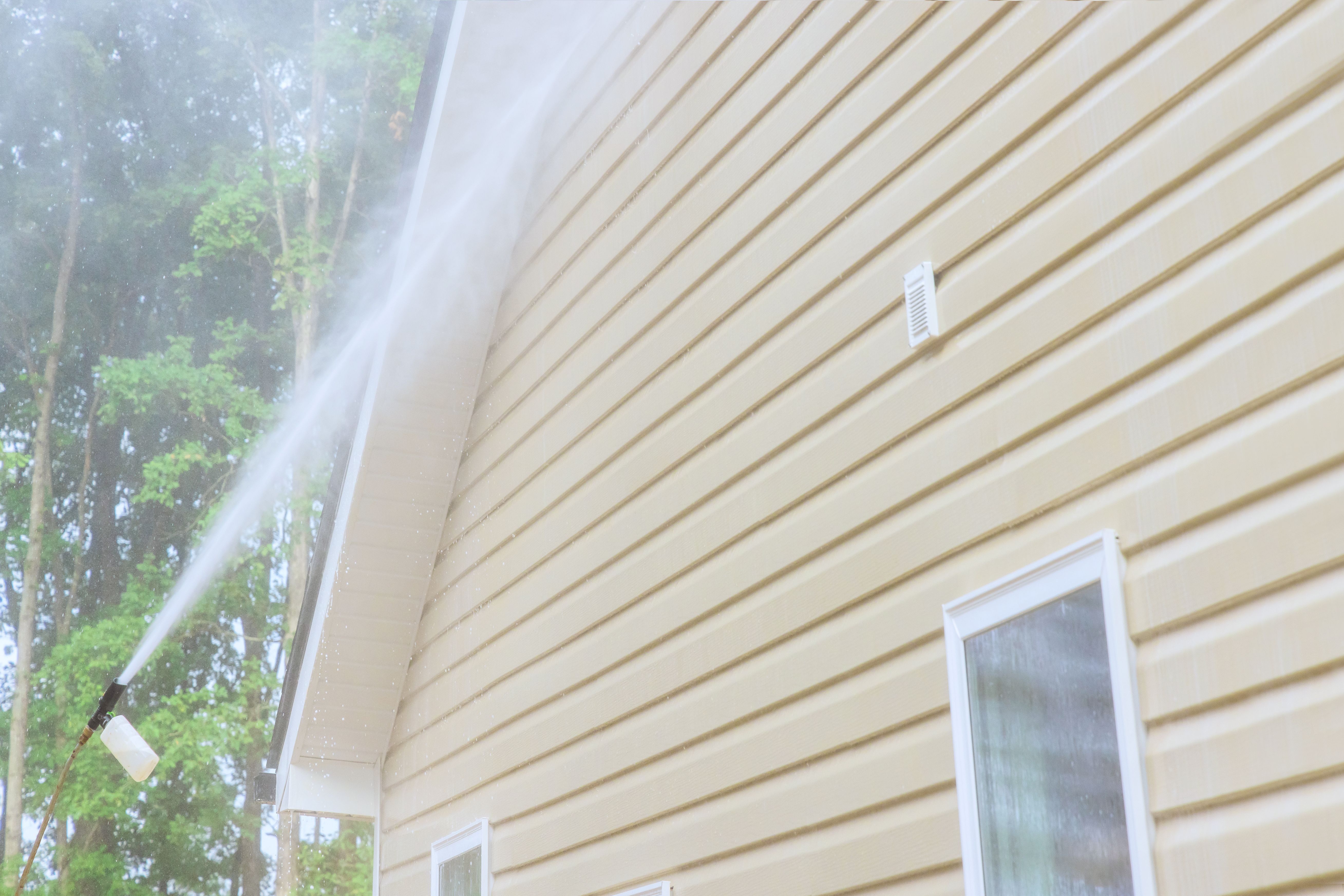 Using high pressure nozzles, service man efficiently washes siding houses with water and soap cleaner