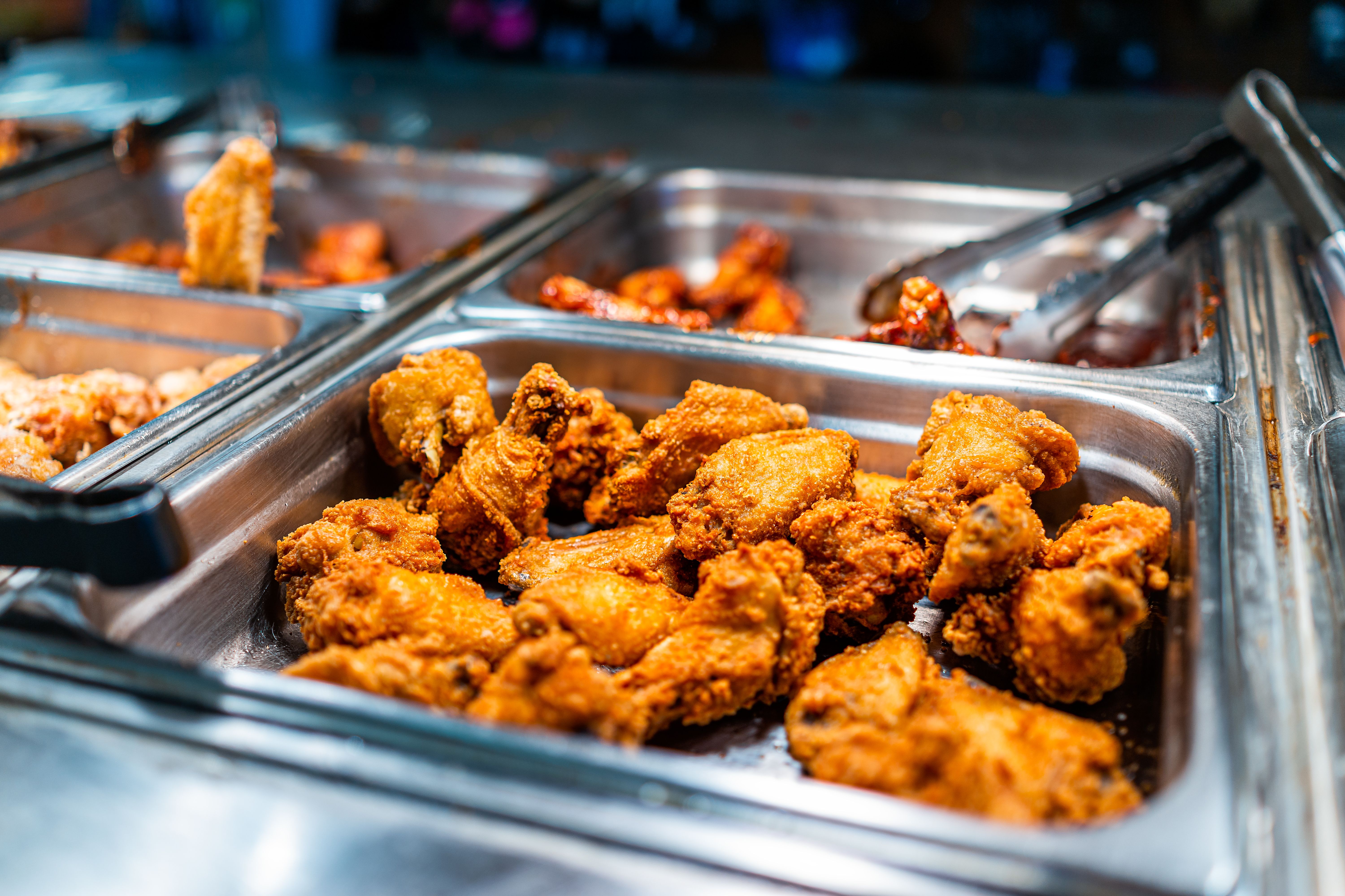 Fried chicken thighs buffet bar self serve with tongs in grocery store, restaurant or catering event with crisp skin and unhealthy food Fried chicken thighs buffet bar self serve with tongs in grocery store, restaurant or catering event with crisp skin and unhealthy food