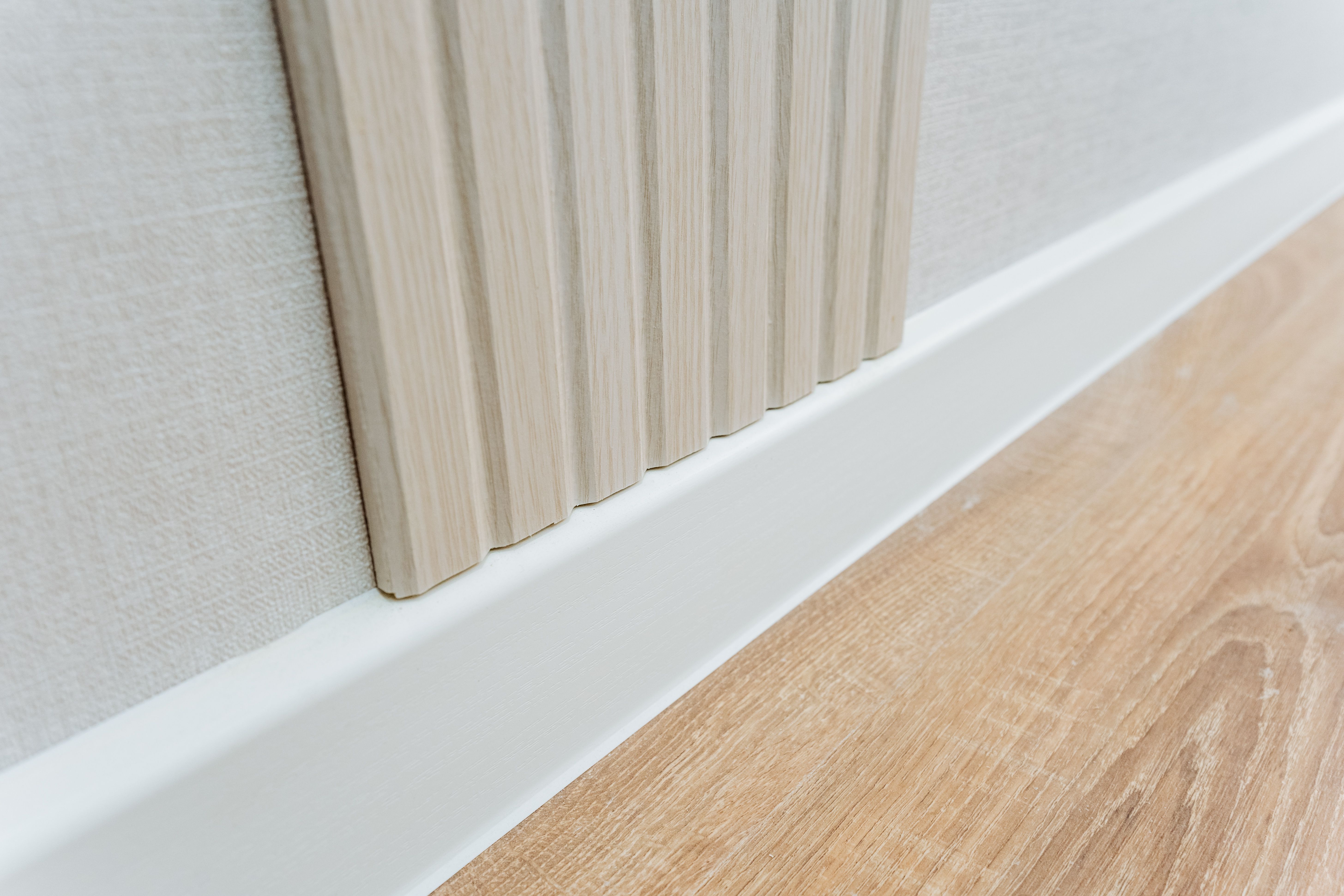 This image features a detailed closeup view of a wall that is adorned with a clean, white trim, alongside a beautifully polished wooden floor that adds character and warmth to the space This image features a detailed closeup view of a wall that is adorned with a clean, white trim, alongside a beautifully polished wooden floor that adds character and warmth to the space