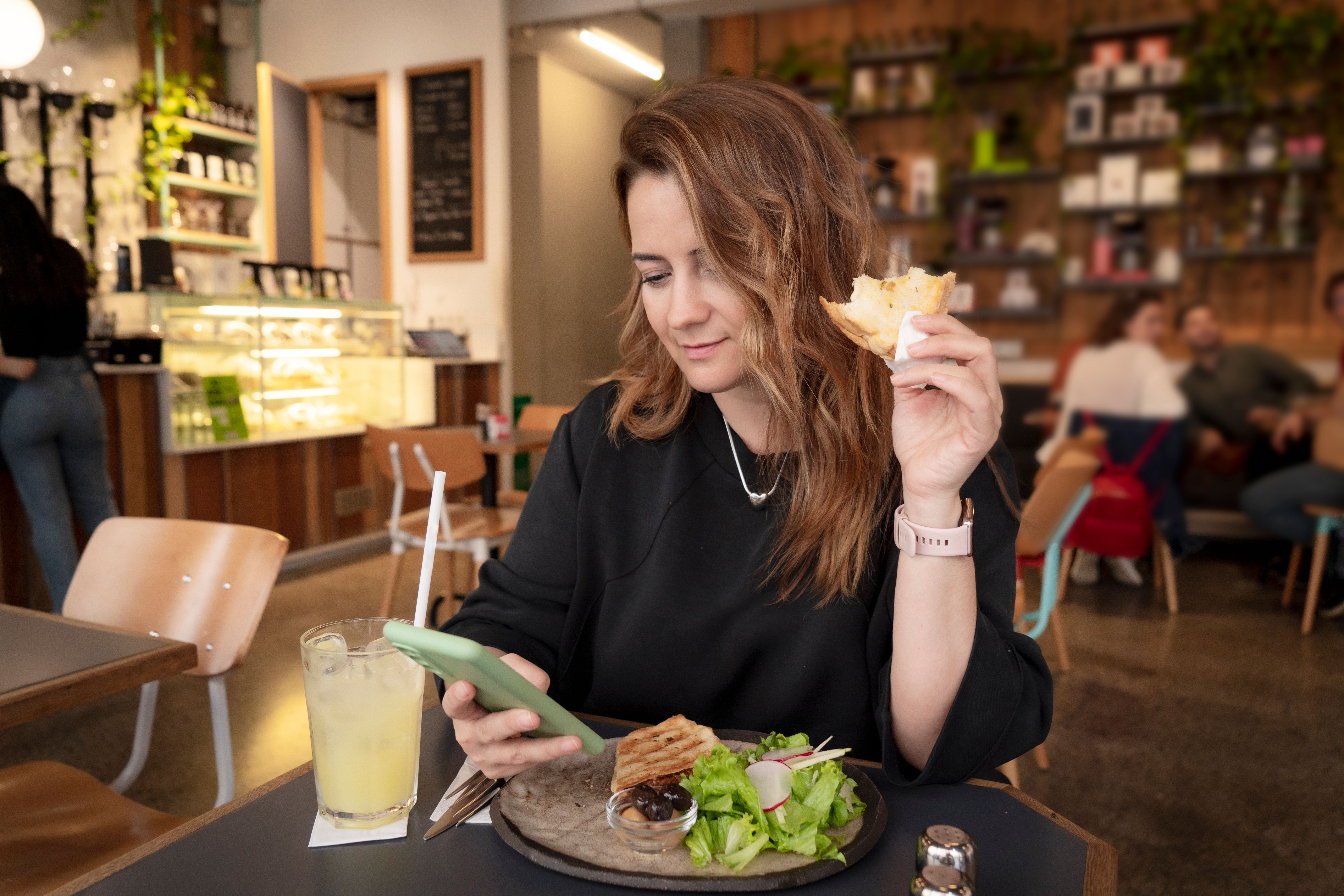 Smiling woman looking at phone while sitting and eating in a cafe