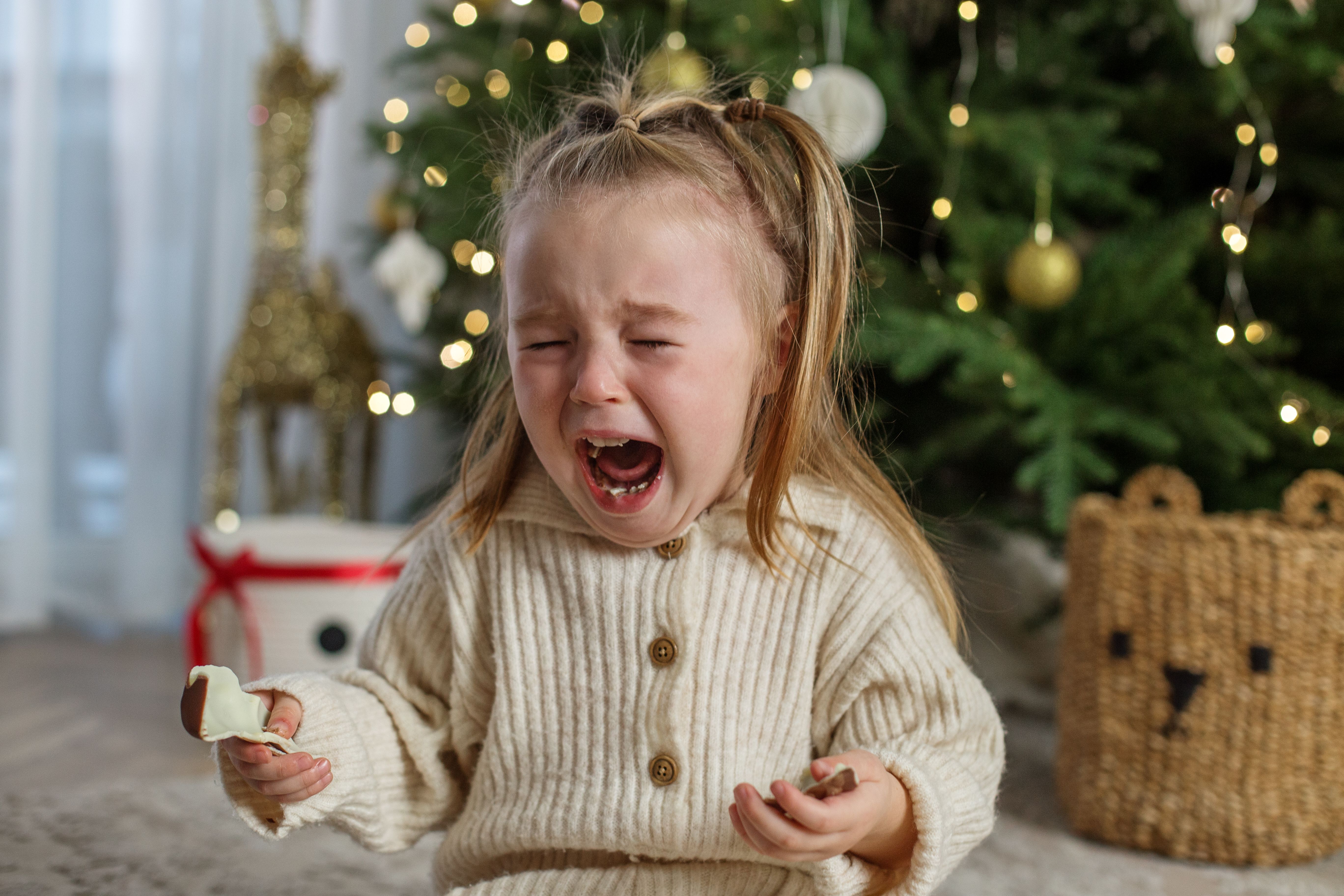 Kid crying while sitting near christmas tree in cozy living room during holiday season